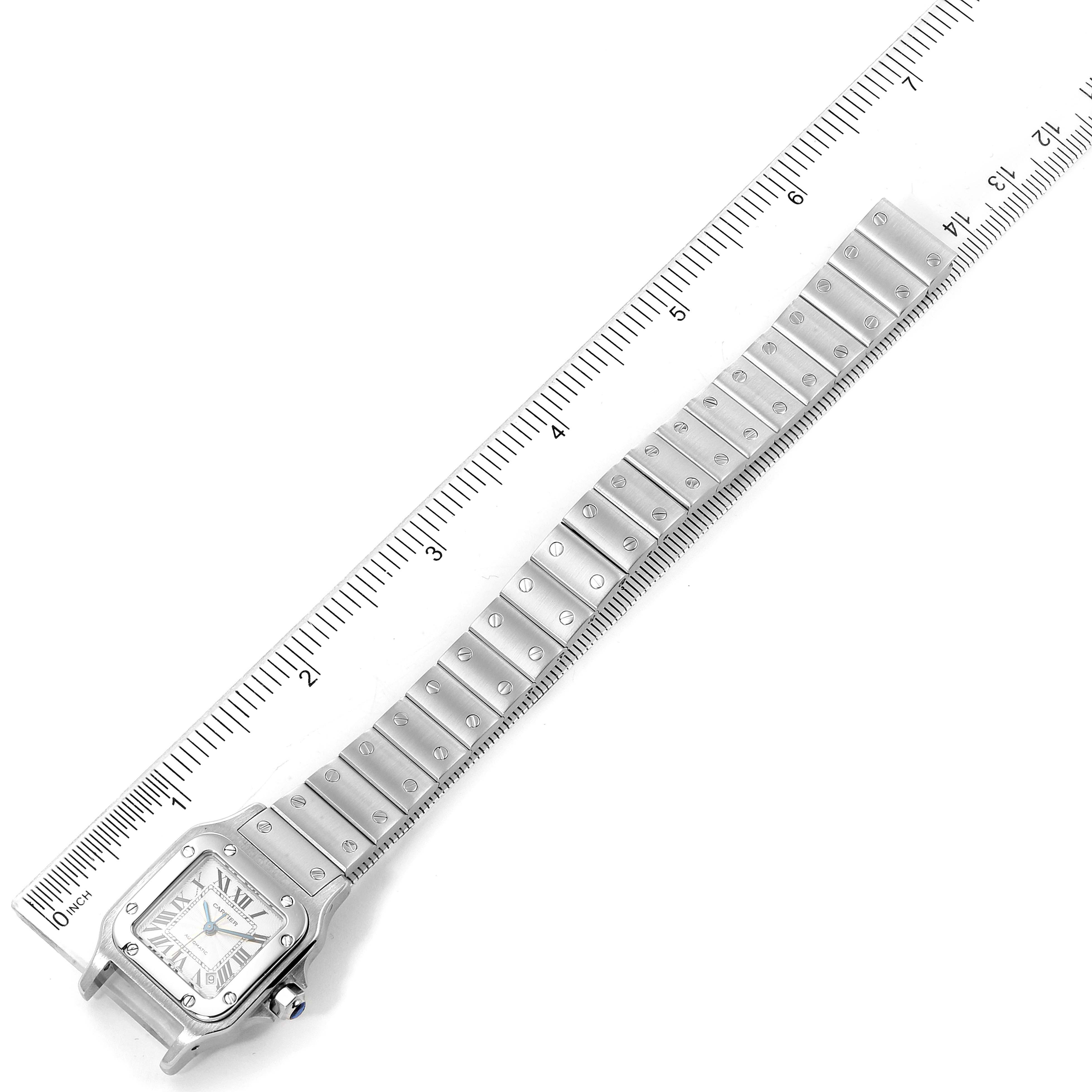 The Santos model by Cartier is shown fully extended with its face and metal bracelet viewed at an angle alongside a ruler.