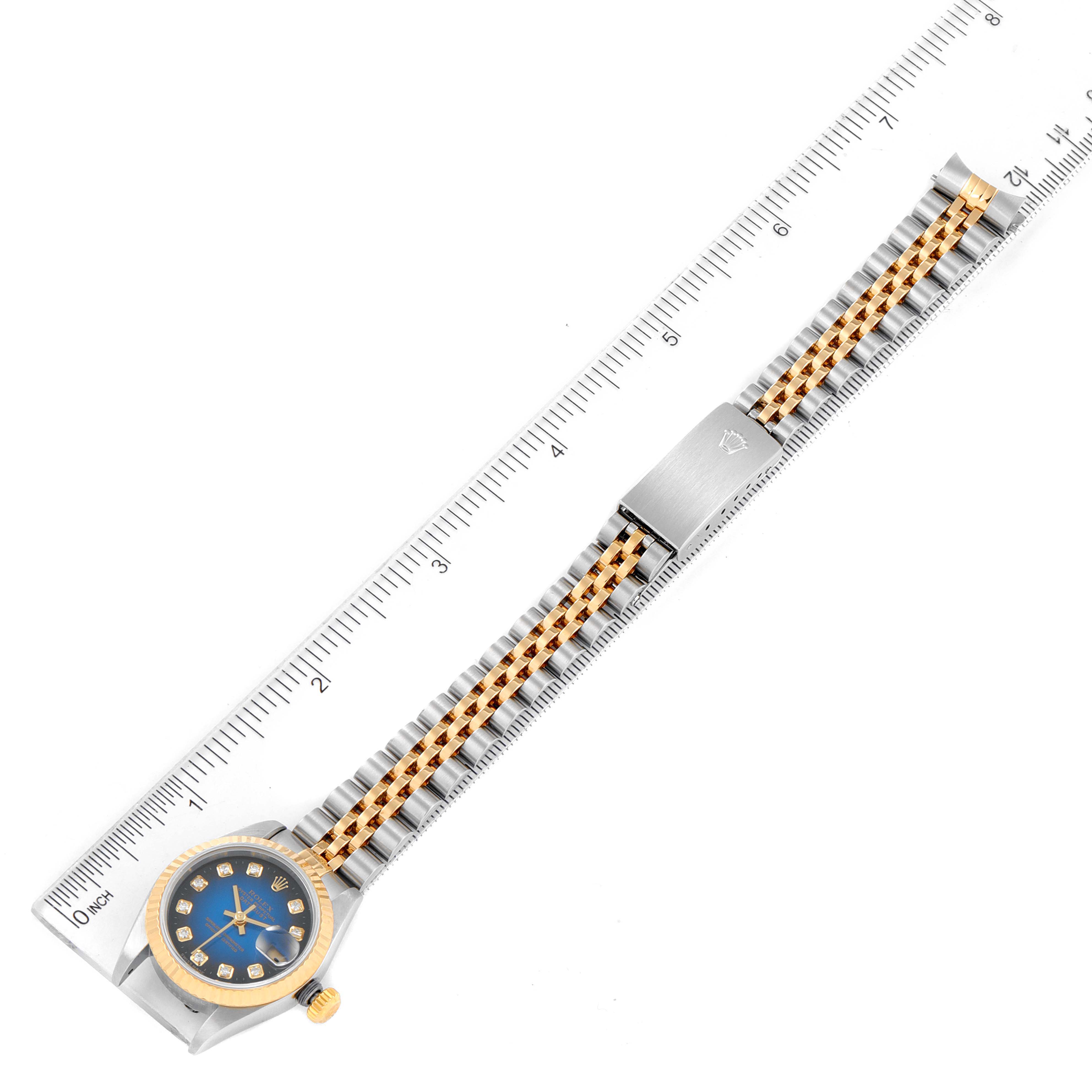 The Rolex Datejust 79173 Women's Steel and Gold (two tone) Blue Dial 79173 Women's Steel and Gold (two tone) Blue Dial watch is shown from an overhead view, highlighting the face, band, and clasp against a measuring ruler.