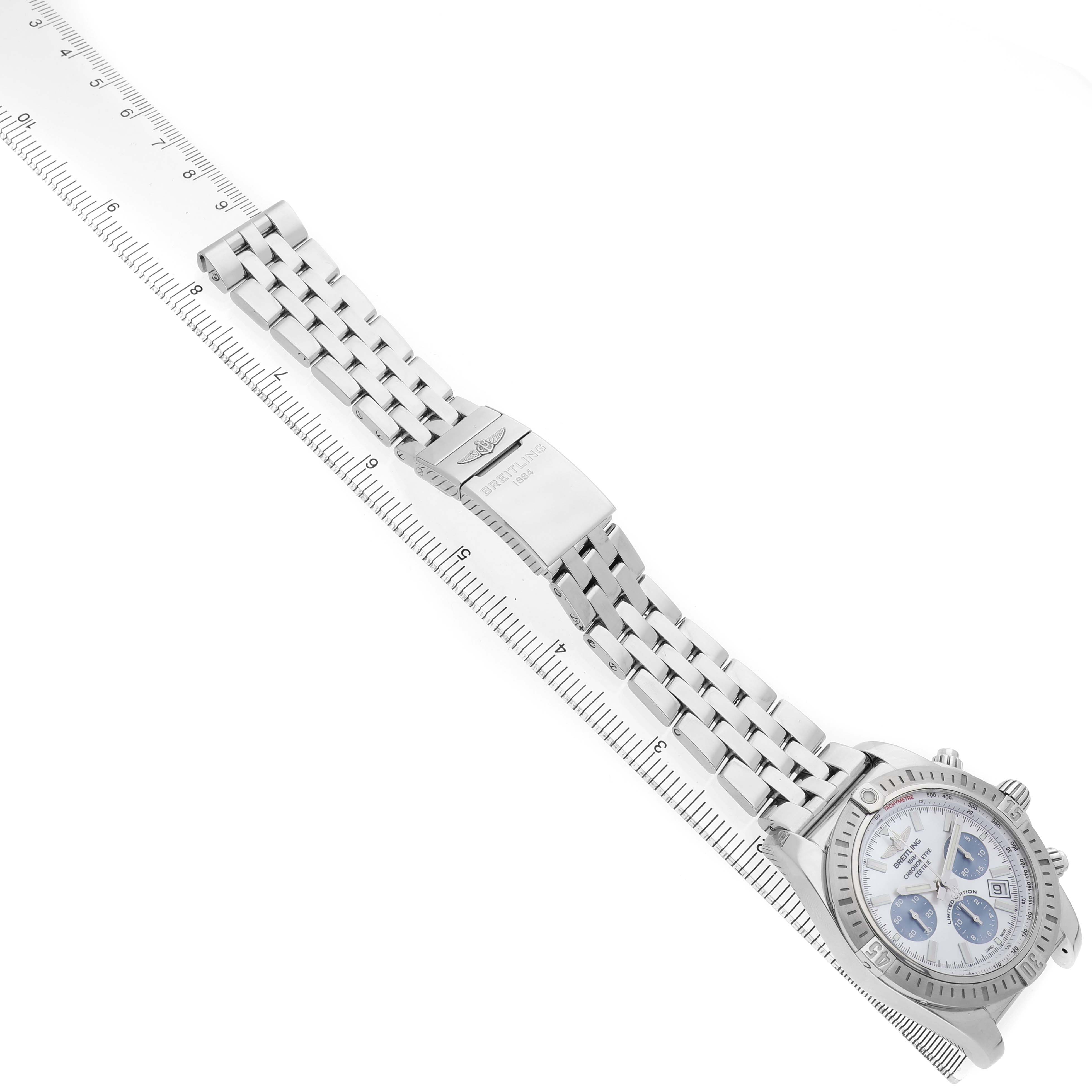 The Breitling Chronomat AB0115 Men's Stainless Steel Mother of Pearl Dial watch is shown diagonally with a focus on its bracelet and clasp beside a measuring ruler.