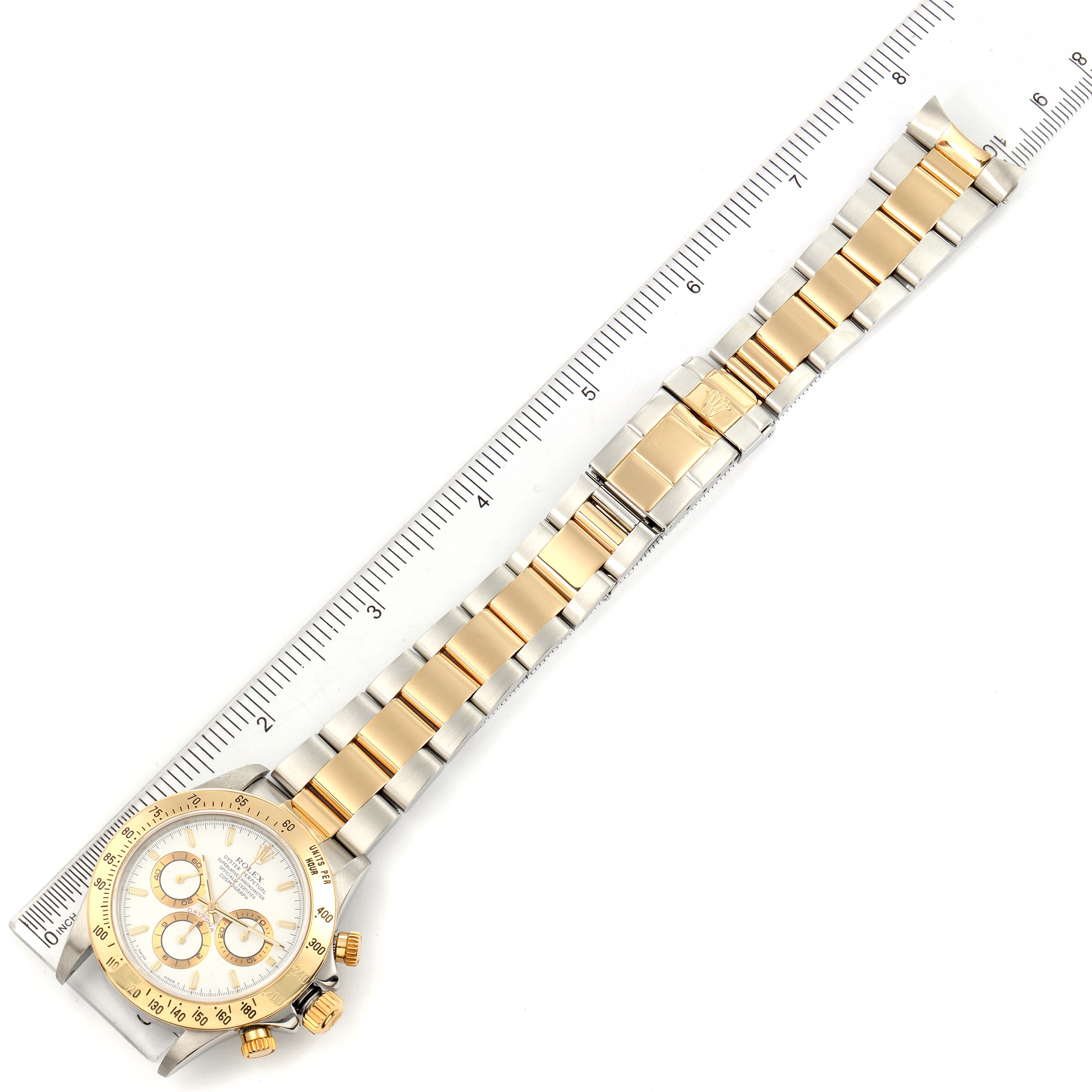 The image shows a Rolex Daytona 16523 Men
s Steel and Gold (two tone) White Dial 16523 Men
s Steel and Gold (two tone) White Dial watch from a top-down angle, featuring its full band and face alongside a ruler for scale.