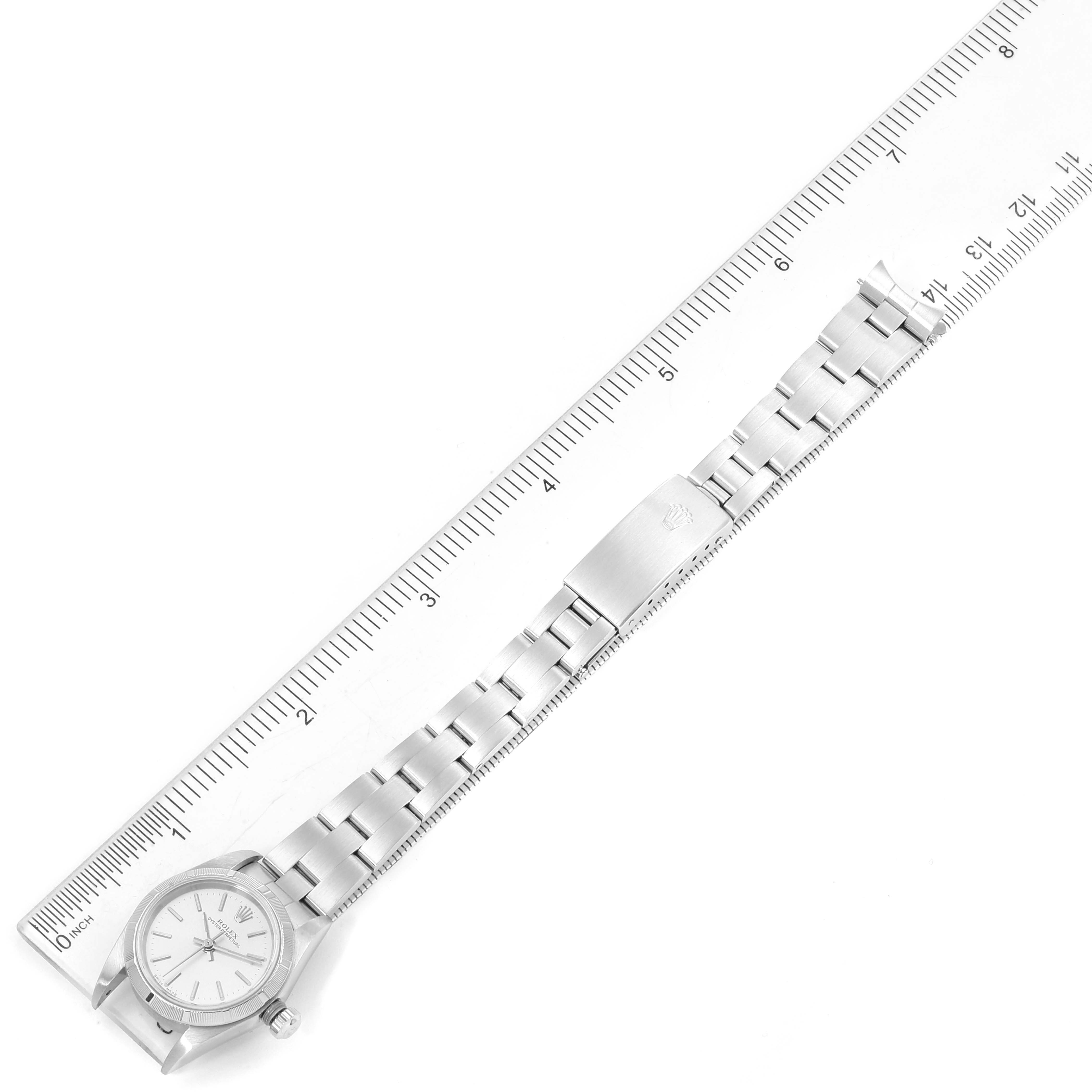 The Rolex Oyster Perpetual 76030 Women's Stainless Steel Silver Dial 76030 Women's Stainless Steel Silver Dial watch is shown laid flat next to a ruler, displaying the watch face, bracelet, and clasp.