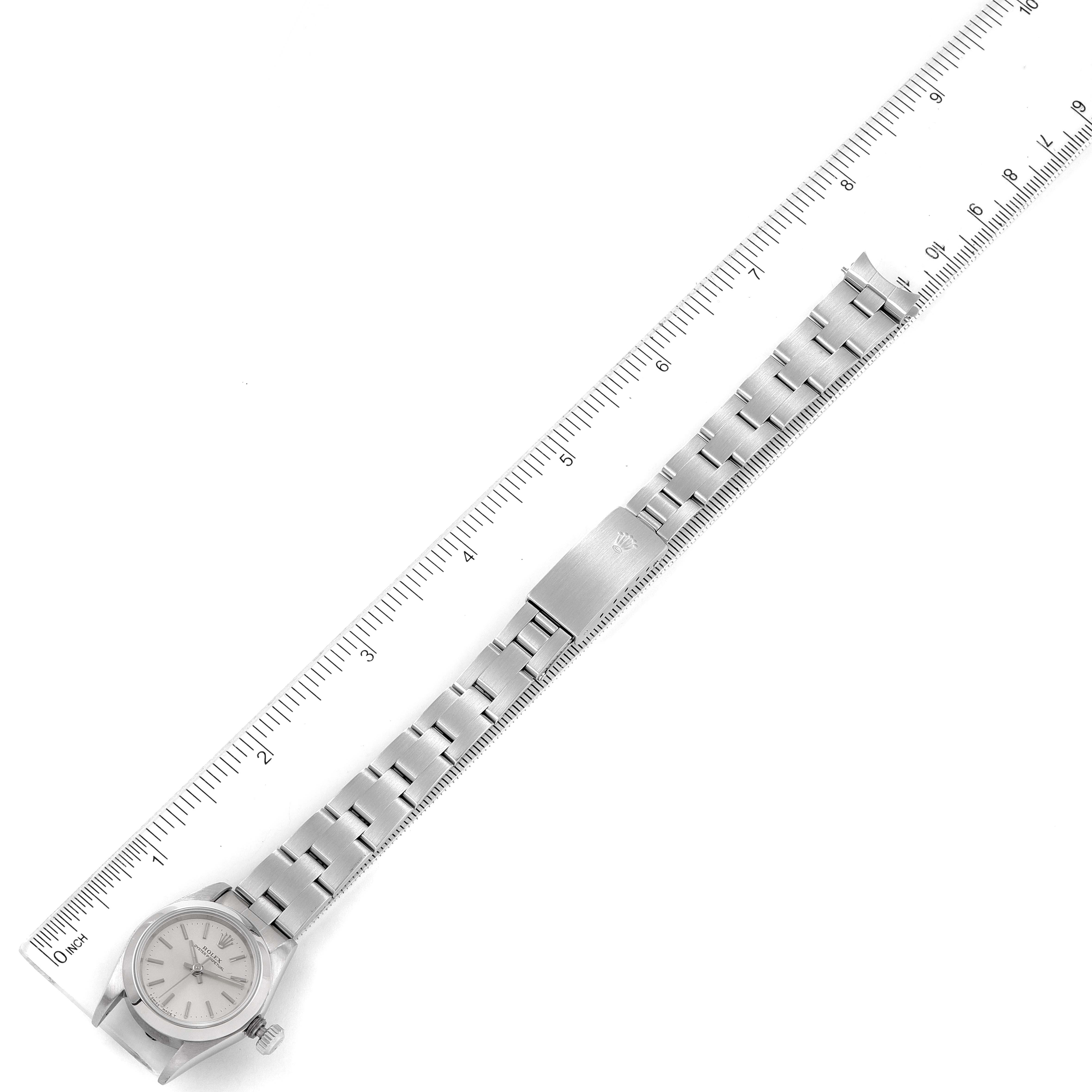 The image shows the face and metal band of a Rolex Oyster Perpetual 67180 Women
s Stainless Steel Silver Dial 67180 Women
s Stainless Steel Silver Dial watch, placed alongside a ruler for scale.