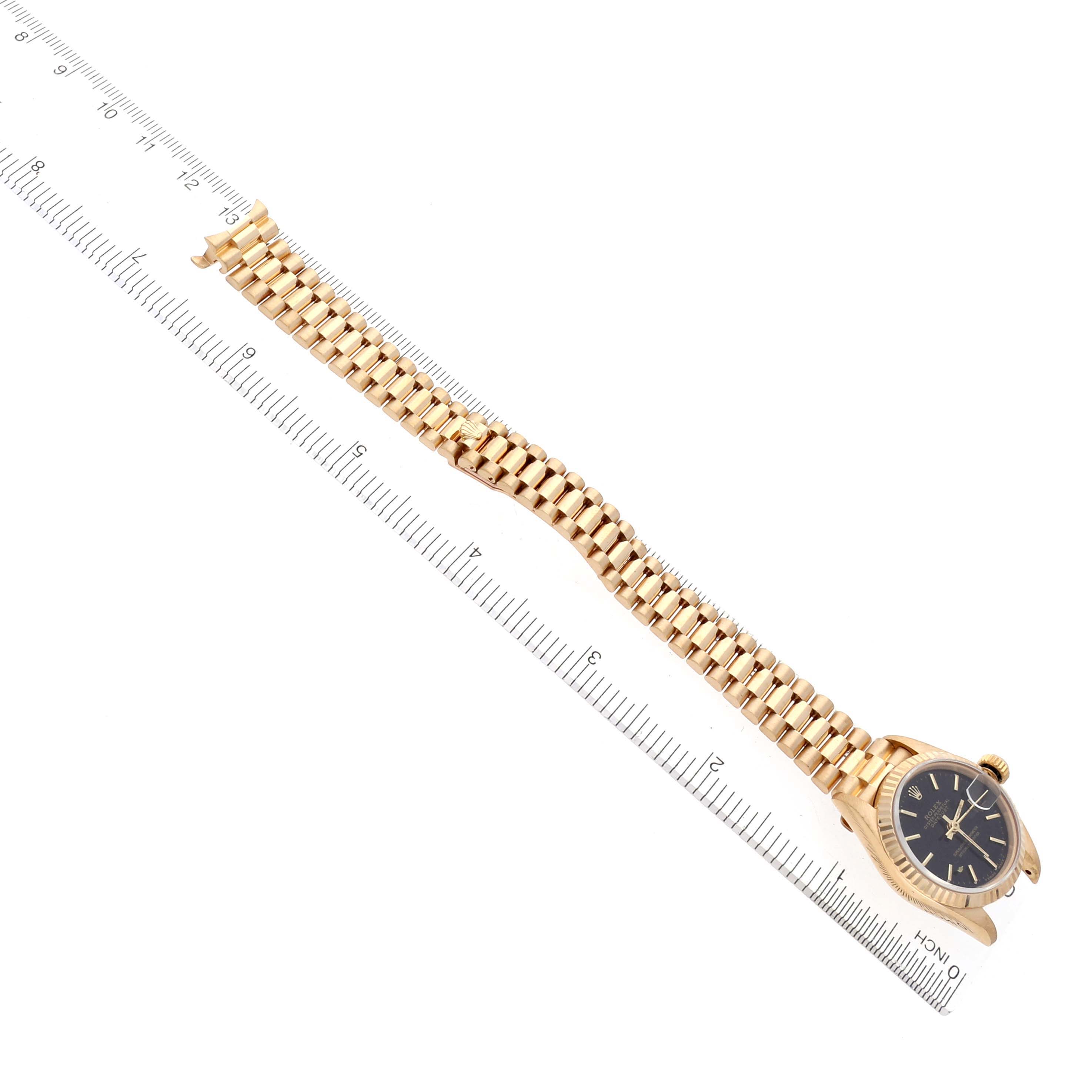 The image shows the Rolex President 69178 Women's Yellow Gold Black Dial 69178 Women's Yellow Gold Black Dial watch partially extended, highlighting the gold bracelet and black dial from a top angle with a ruler for scale.