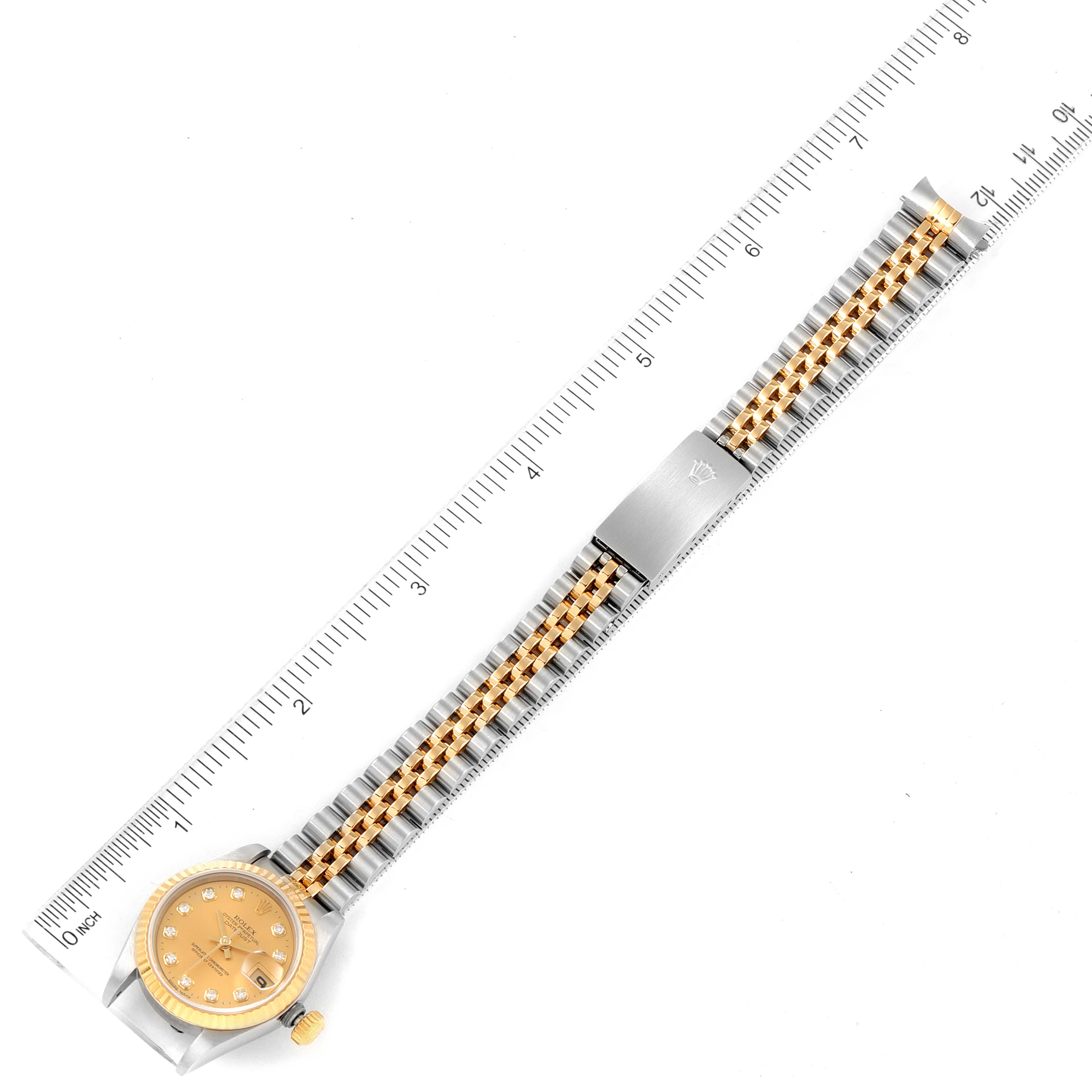 The image shows a Rolex Datejust 69173 Women
s Steel and Gold (two tone) Champagne Dial 69173 Women
s Steel and Gold (two tone) Champagne Dial watch laid flat, displaying its face, band, and clasp alongside a ruler for scale.