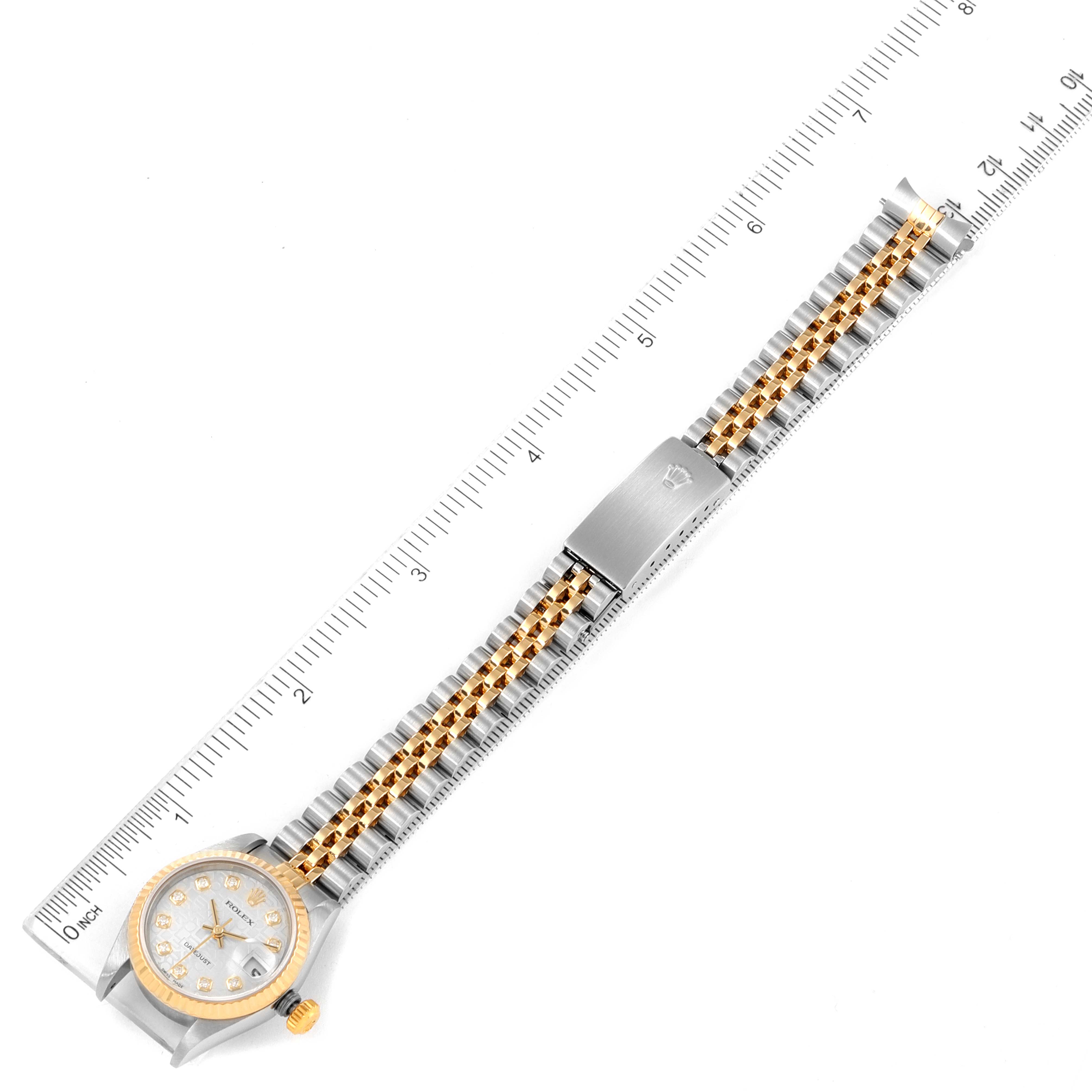 The image shows a top view of a Rolex Datejust 79173 Women
s Steel and Gold (two tone) Silver Dial 79173 Women
s Steel and Gold (two tone) Silver Dial watch, featuring its dial, case, and metal bracelet next to a ruler.