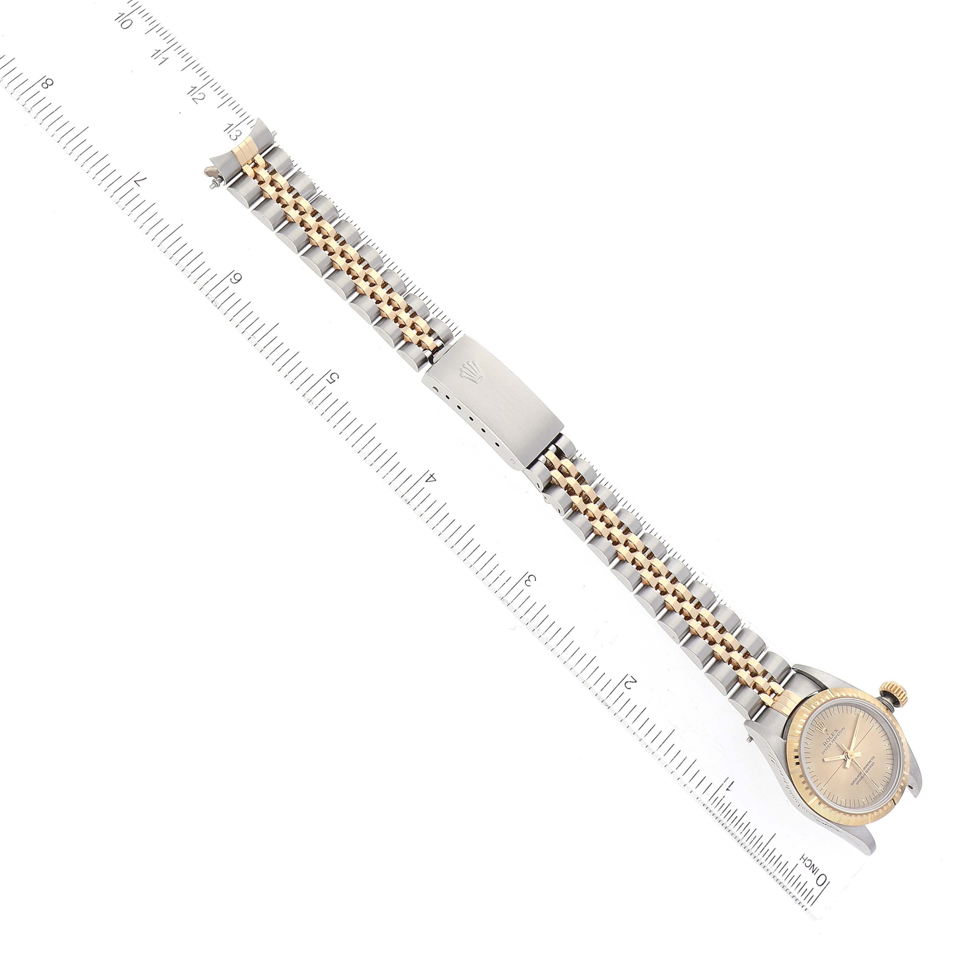 The Rolex Oyster Perpetual 67243 Women's Steel and Gold (two tone) Champagne Dial 67243 Women's Steel and Gold (two tone) Champagne Dial watch is shown in a top-down angle, featuring its gold and silver bracelet and clasp.