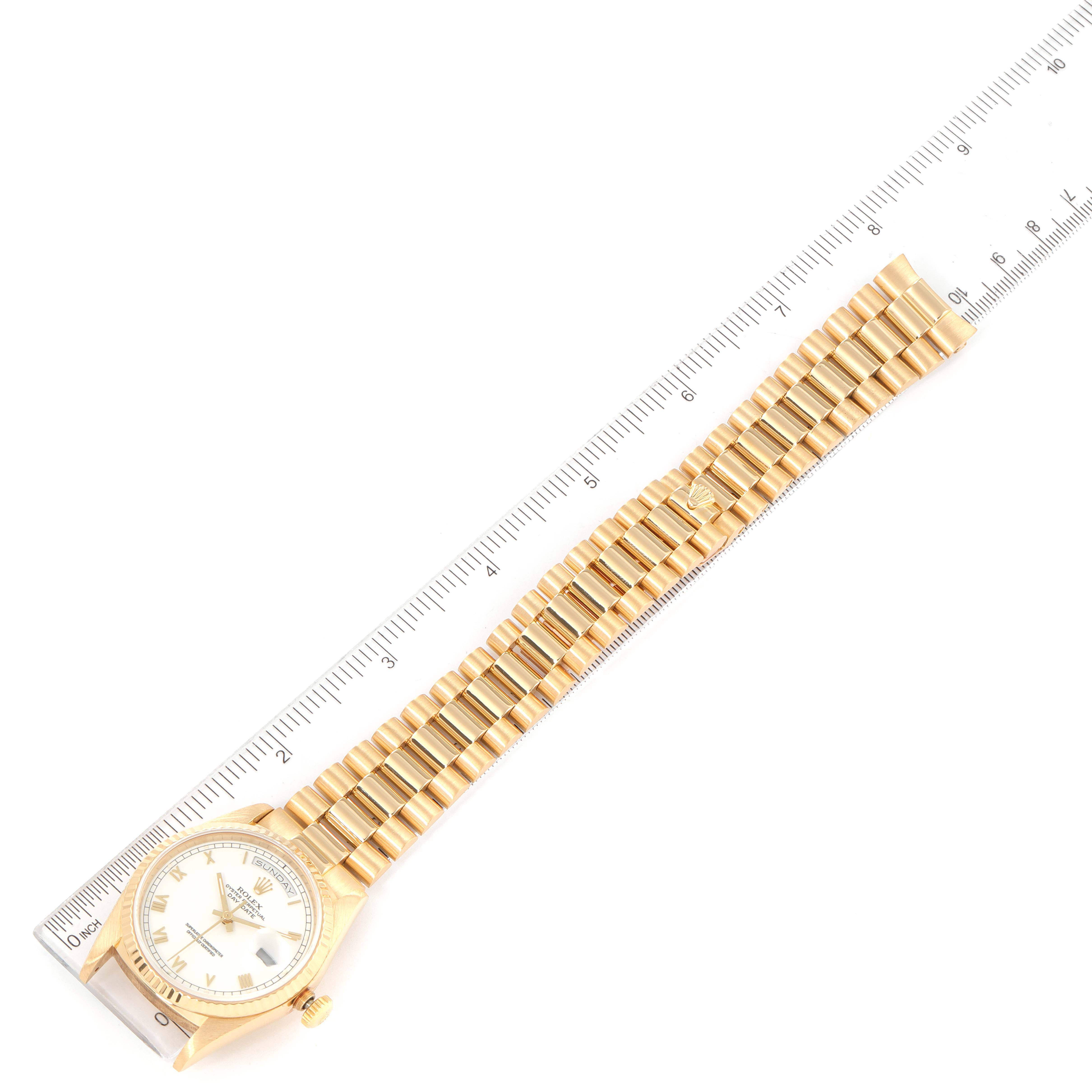The image shows a top-view angle of a Rolex President 18238 Men
s Yellow Gold White Dial 18238 Men
s Yellow Gold White Dial model watch with its gold bracelet fully extended alongside a ruler.