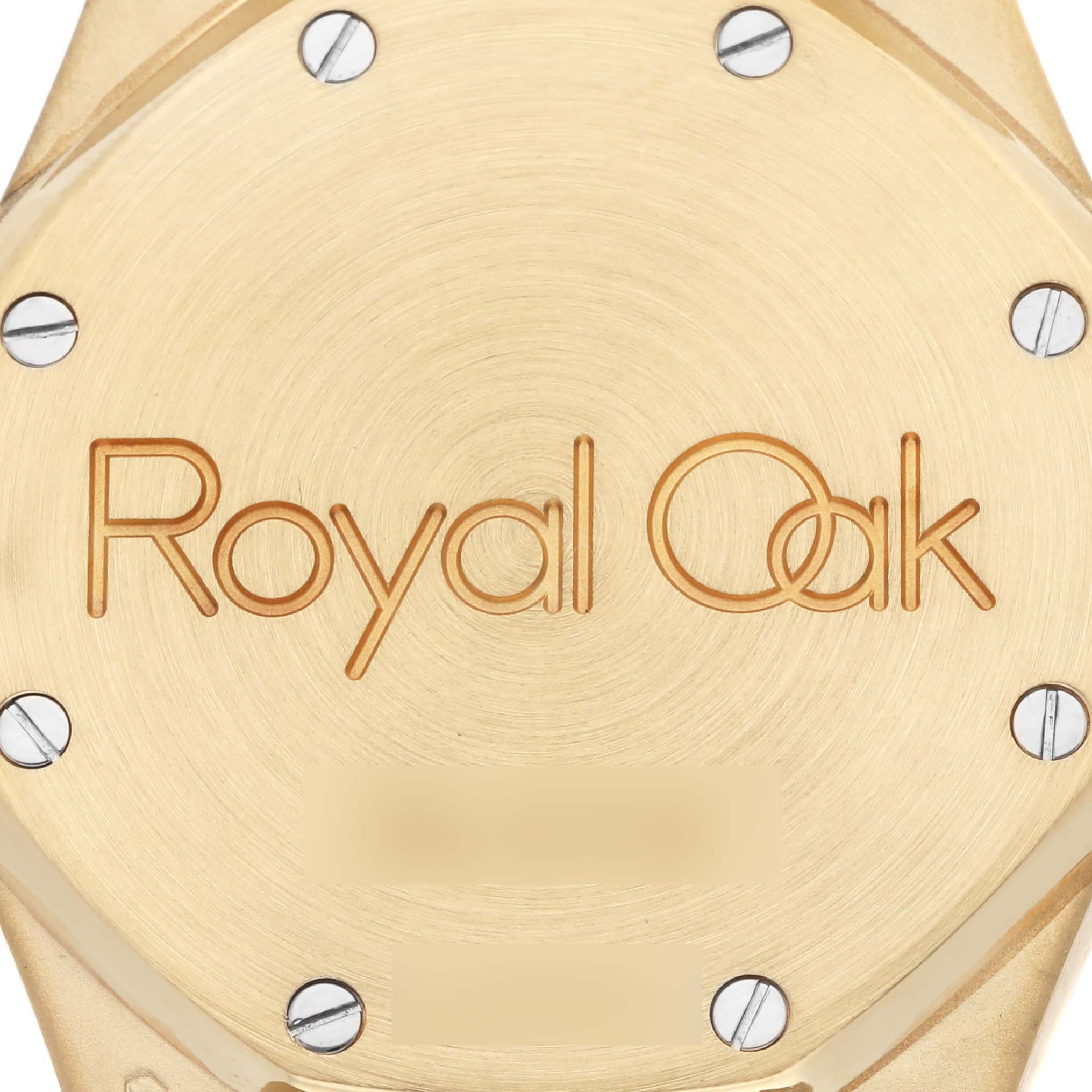 The image shows a close-up of the gold case back of an Audemars Piguet Royal Oak 25730BA.OO.0789BA.06 Men's Yellow Gold Silver Dial 25730BA.OO.0789BA.06 Men's Yellow Gold Silver Dial, highlighting the engraved logo and screws.
