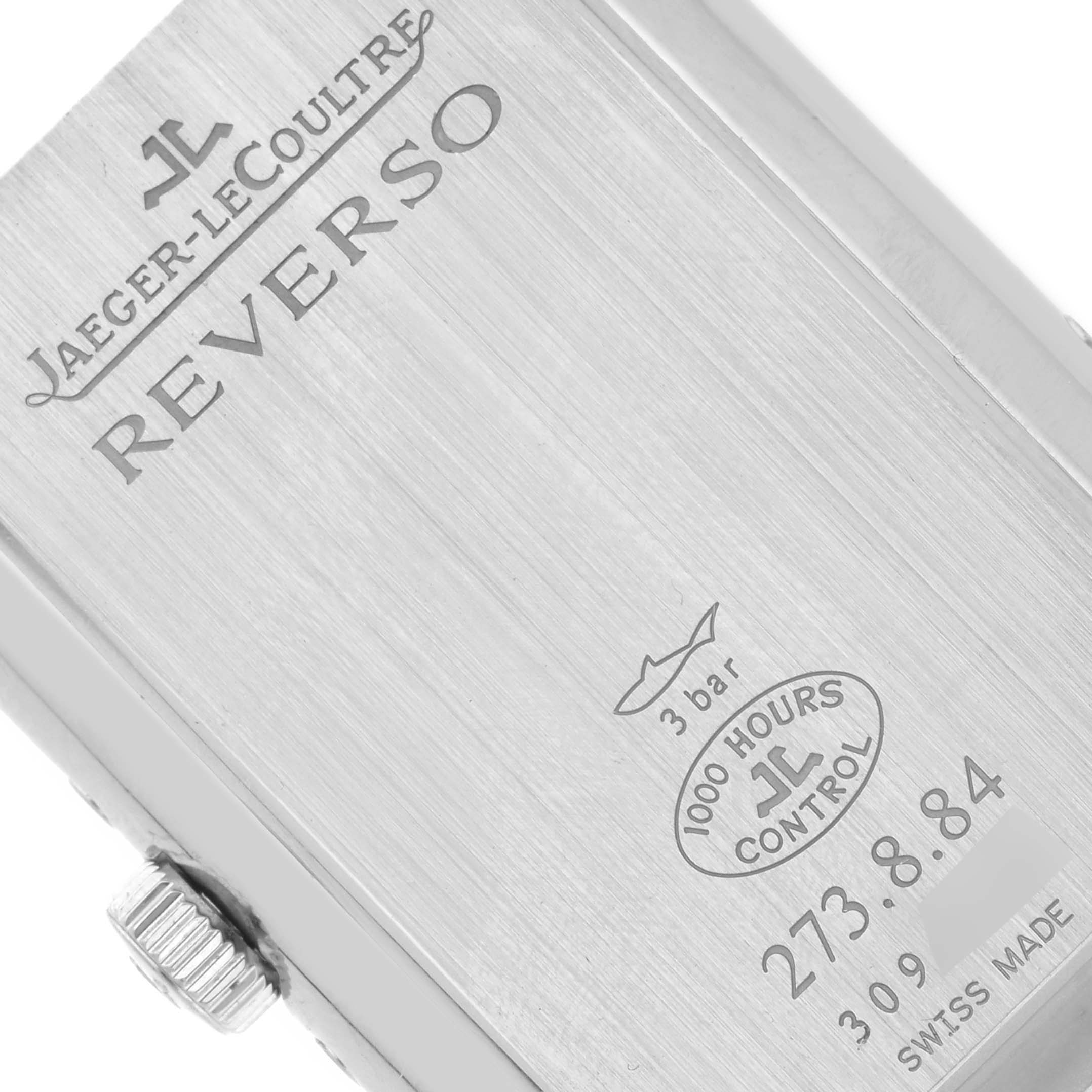 The image shows the back of a Jaeger-LeCoultre Reverso watch, highlighting its engravings and crown from a slightly angled perspective.