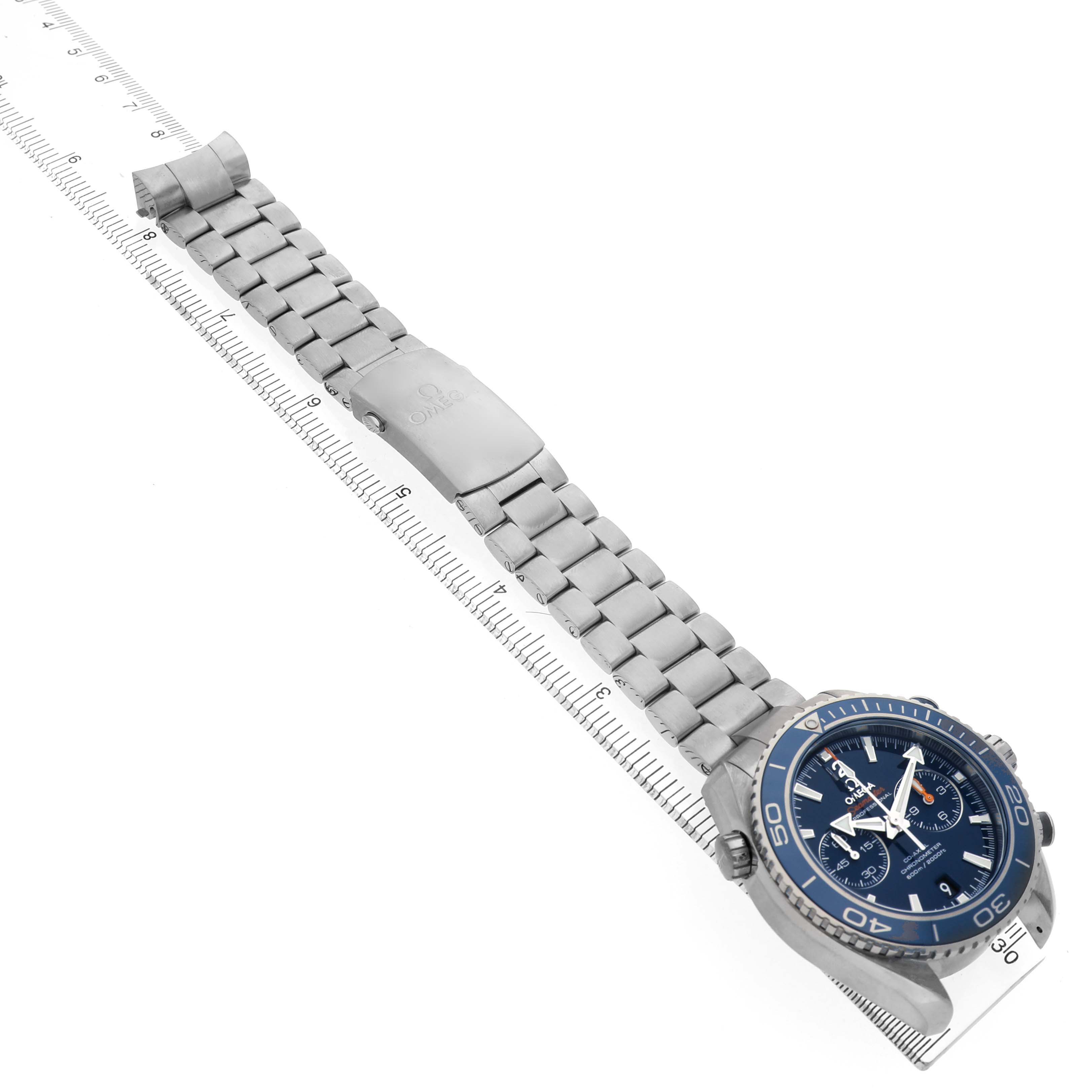 The Omega Planet Ocean 232.90.46.51.03.001 Men's Titanium Blue Dial watch is shown at an angle displaying the face, bracelet, and clasp, resting on a ruler.