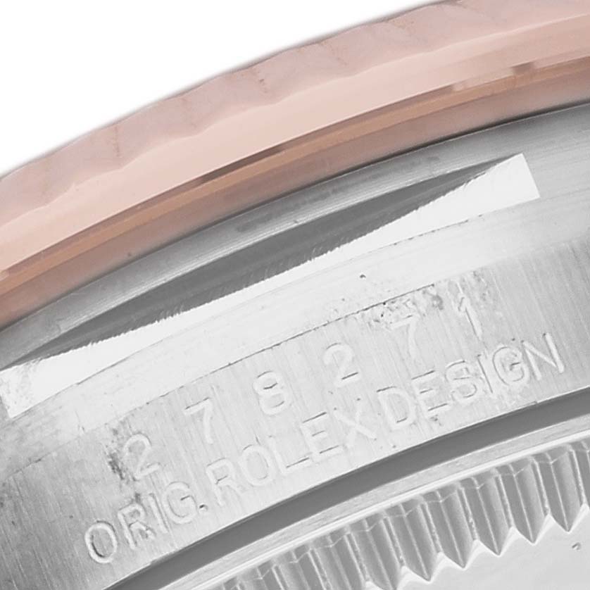 This close-up image of a Rolex Mid-Size 278271 Women's Steel and Gold (two tone) Pink Dial 278271 Women's Steel and Gold (two tone) Pink Dial watch shows part of the bezel and case with engraved serial numbers and "ORIG.ROLEXDESIGN".