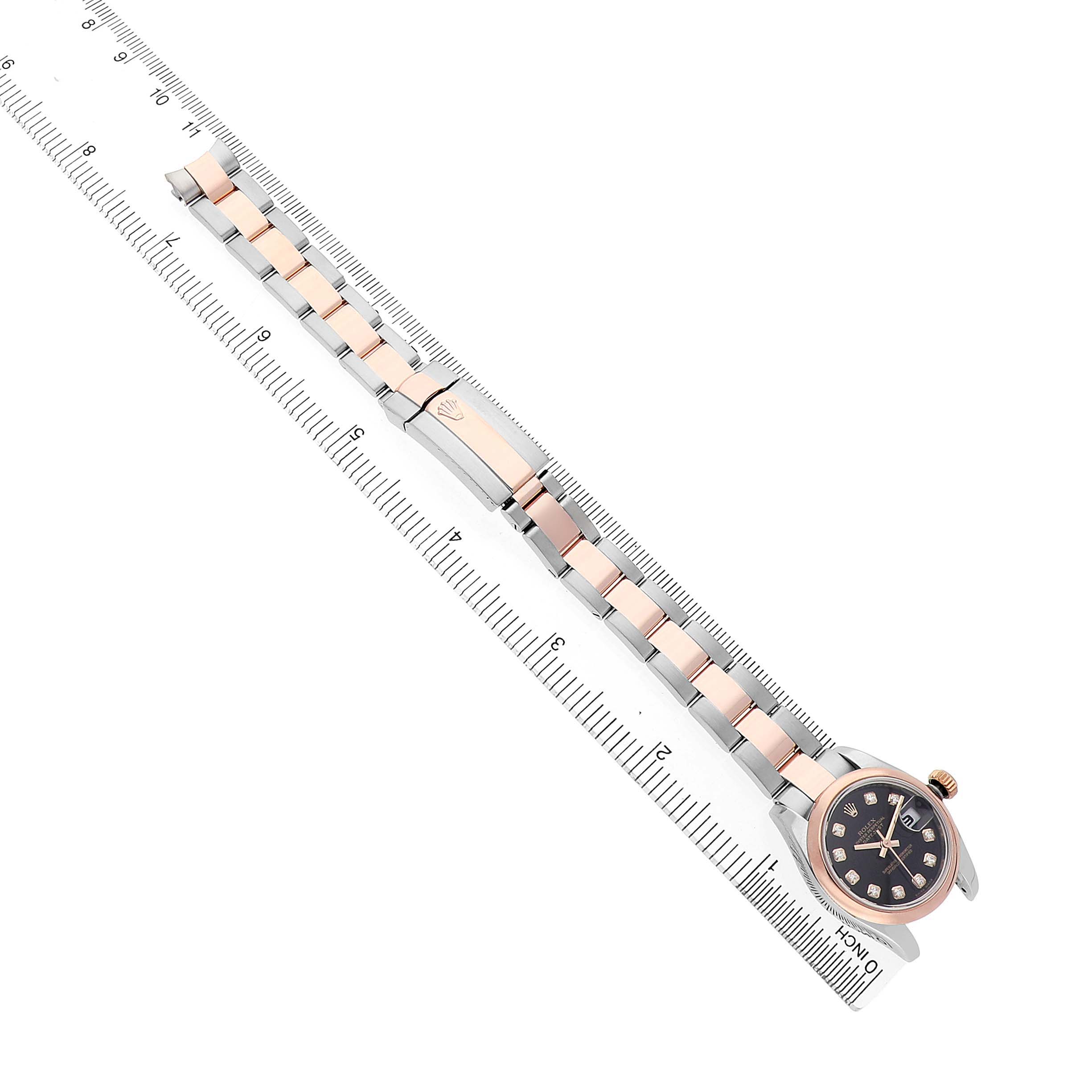 The Rolex Datejust 179161 Women's Steel and Gold (two tone) Black Dial is shown from a top view, displaying the full watch face, bracelet, and clasp on a ruler.