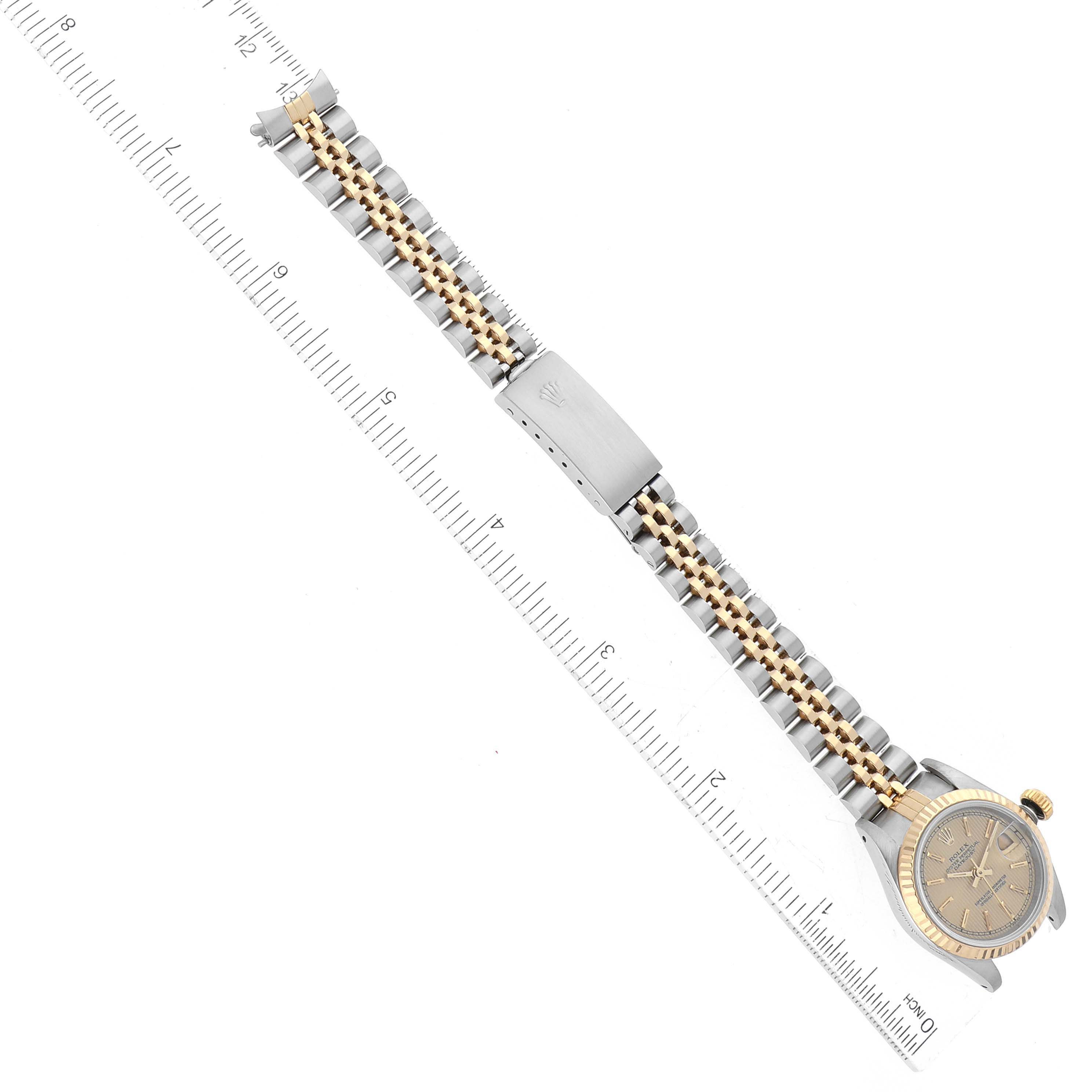 The Rolex Datejust 69173 Women's Steel and Gold (two tone) Champagne Dial 69173 Women's Steel and Gold (two tone) Champagne Dial watch is shown from a top-down angle, highlighting its face, bracelet, and clasp with a measuring ruler beside it.