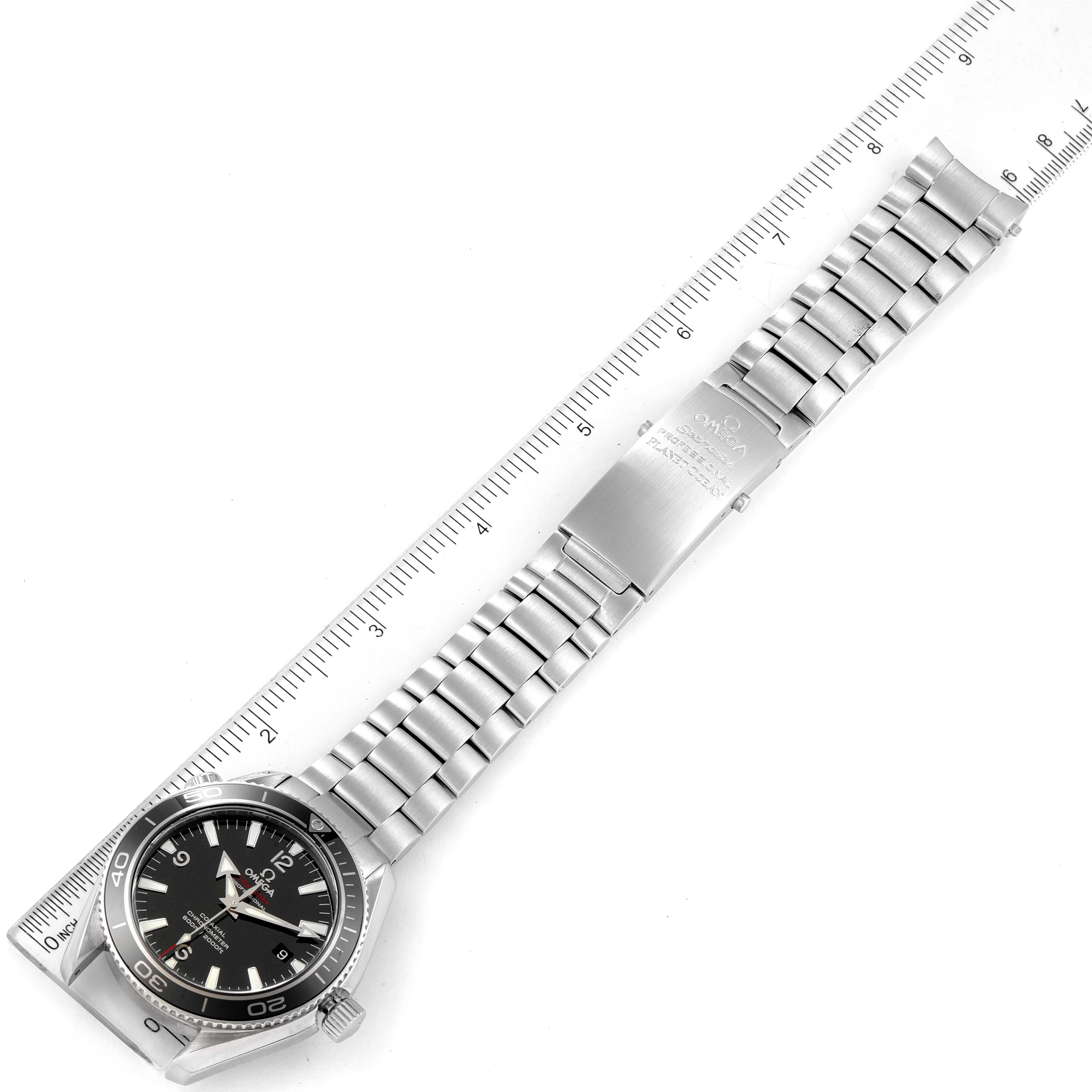 This image shows an Omega Planet Ocean 222.30.42.20.01.001 Men's Stainless Steel Black Dial 222.30.42.20.01.001 Men's Stainless Steel Black Dial watch laid flat next to a ruler, displaying the entire watch including the face, bracelet, and clasp.