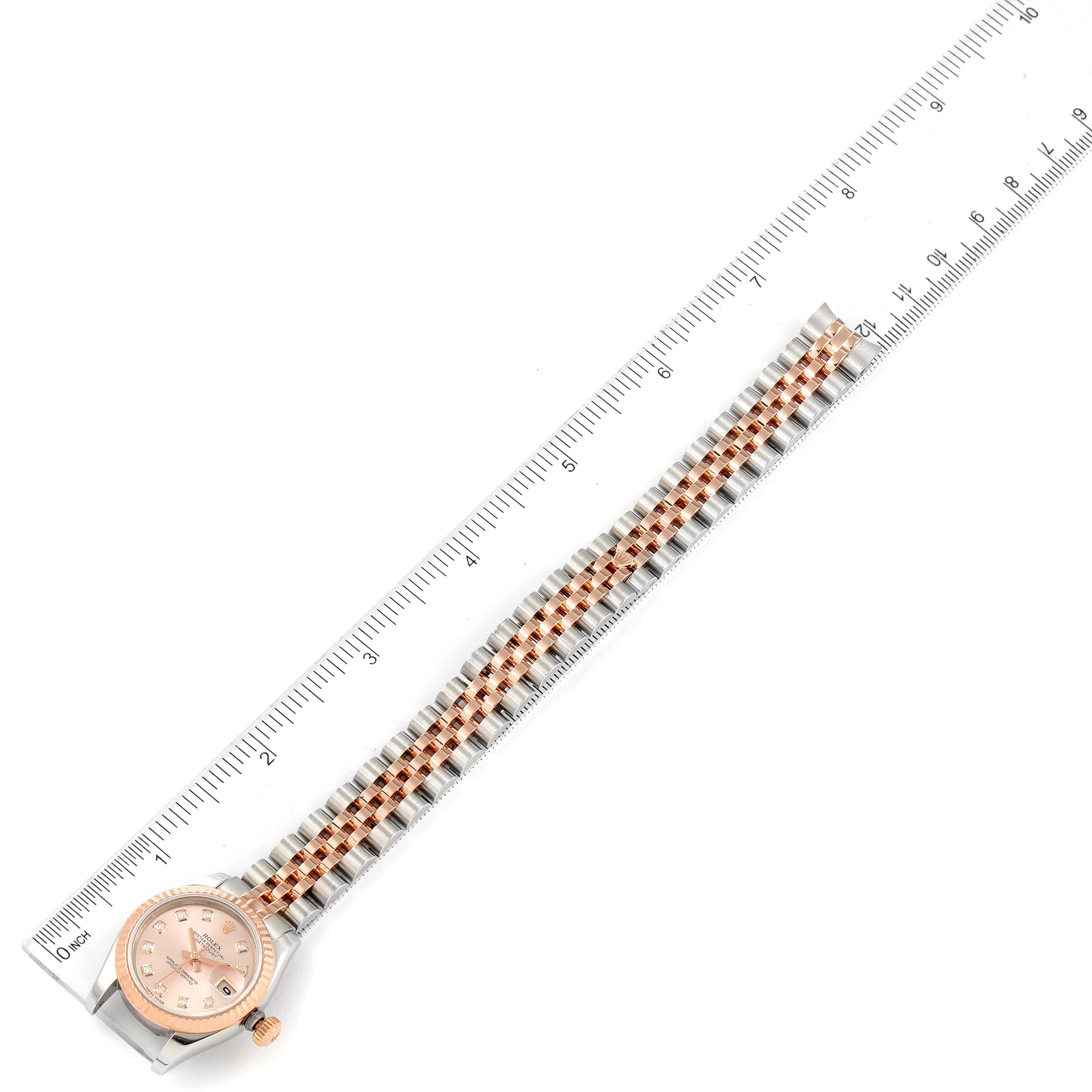 The image shows a Rolex Datejust 179171 Women's Steel and Gold (two tone) Pink Dial 179171 Women's Steel and Gold (two tone) Pink Dial watch horizontally aligned next to a ruler, displaying the face and the full length of its bracelet.