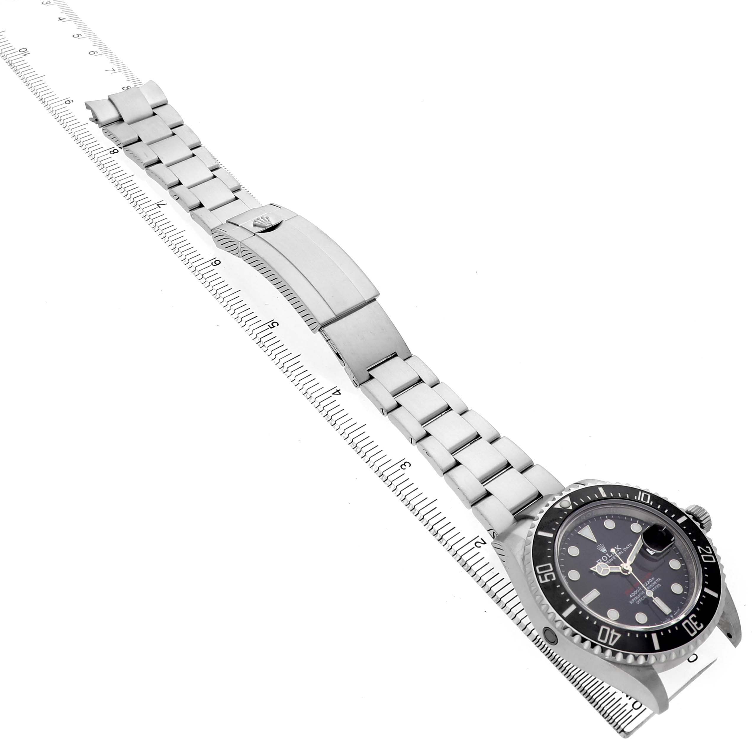 The Rolex Sea-Dweller 126600 Men's Stainless Steel Black Dial watch is shown at an angle, displaying the face, bezel, bracelet, and clasp with a measuring ruler beside it.