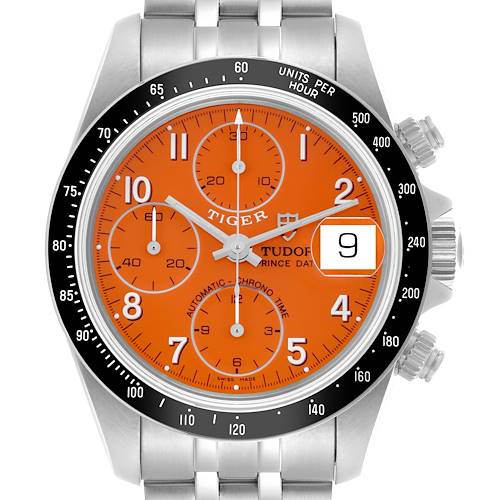 The Tudor Tiger model watch is shown from the front, displaying the orange dial, chronograph subdials, and date window.