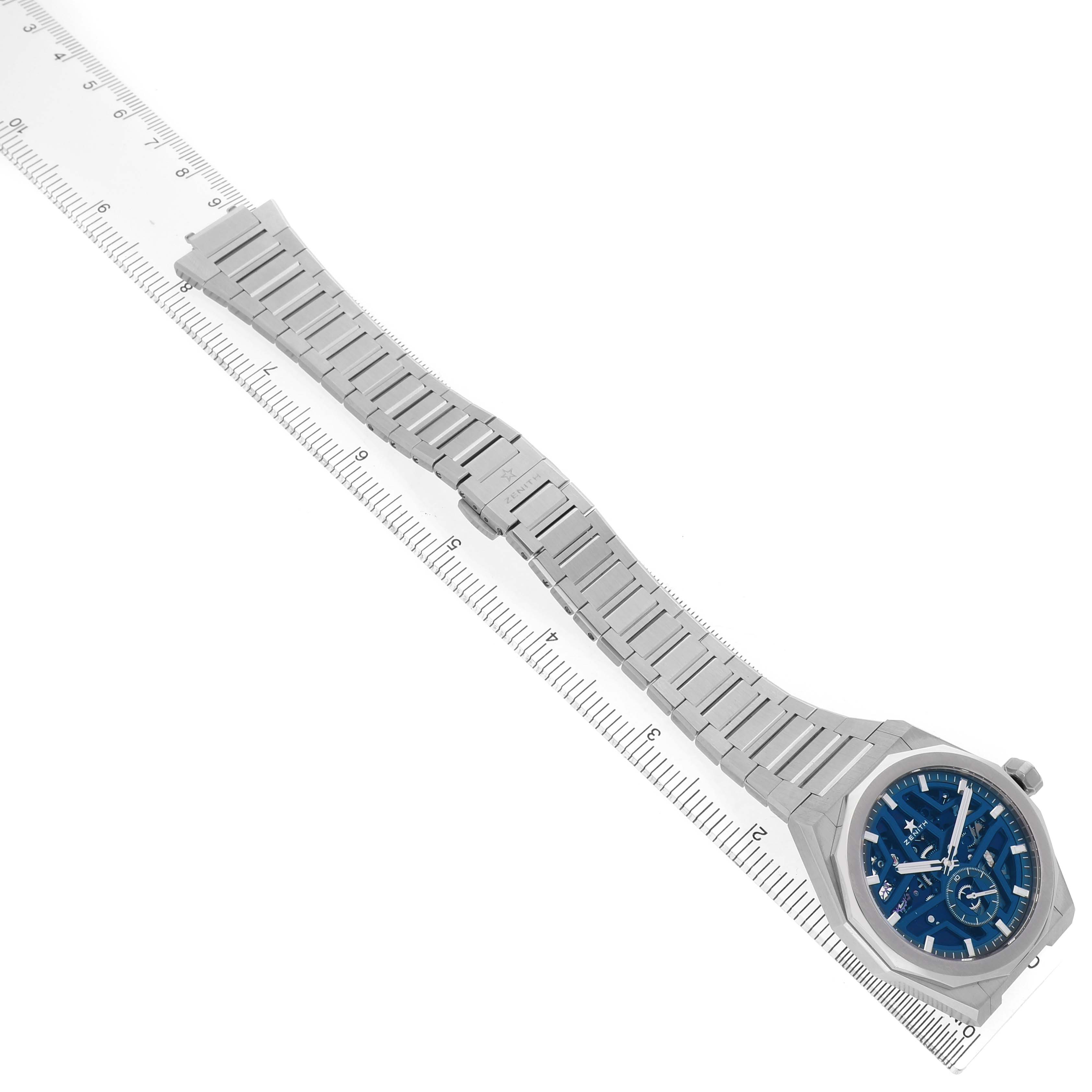 The Zenith Defy 03.9300.3620 / 79.I001 Men's Stainless Steel Blue Dial watch is shown at an angled view, highlighting the case, dial, and full bracelet against a ruler.