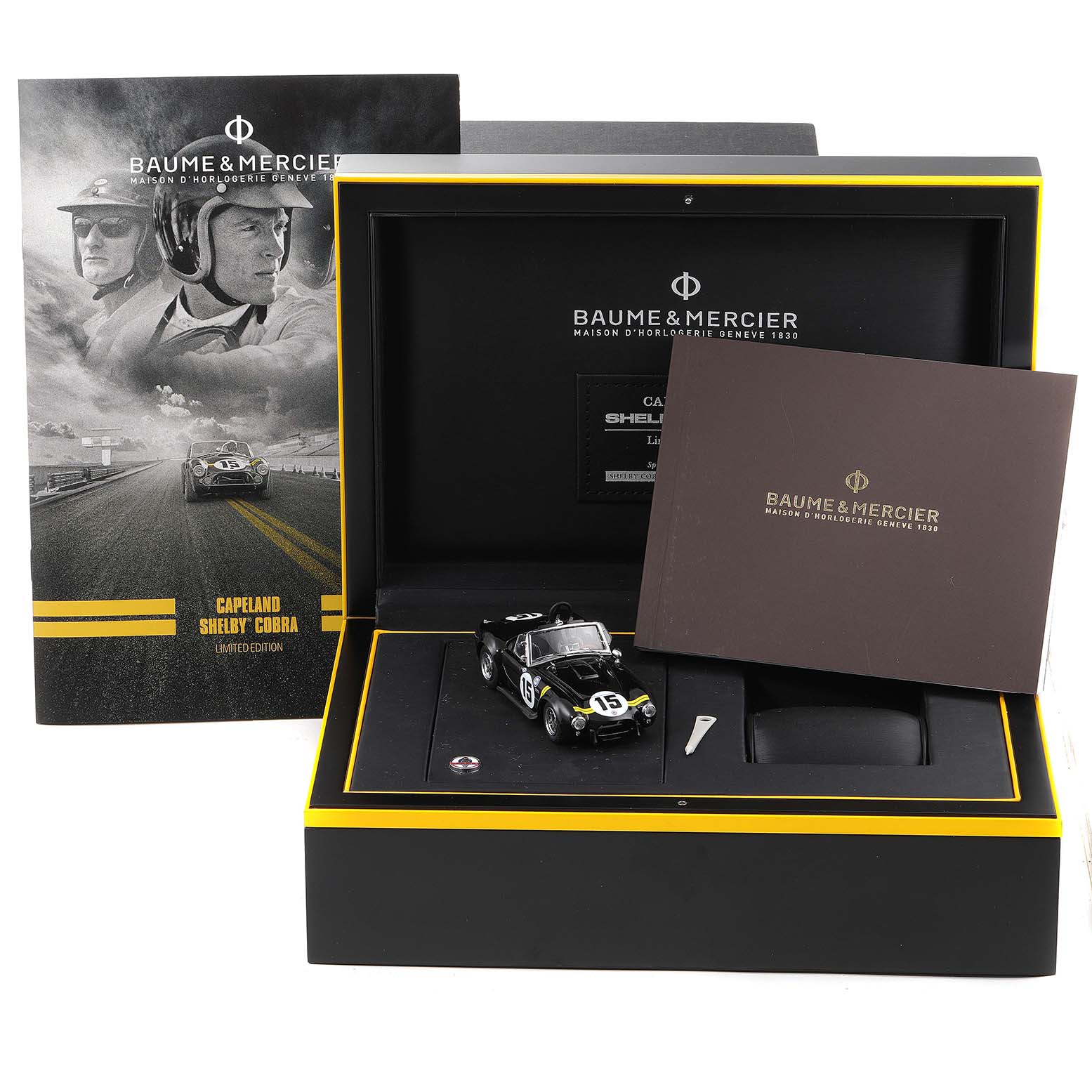This image shows the packaging and accessories for the Baume & Mercier Capeland 65798 Men's Stainless Steel Black Dial 65798 Men's Stainless Steel Black Dial model, including a miniature car and booklets.
