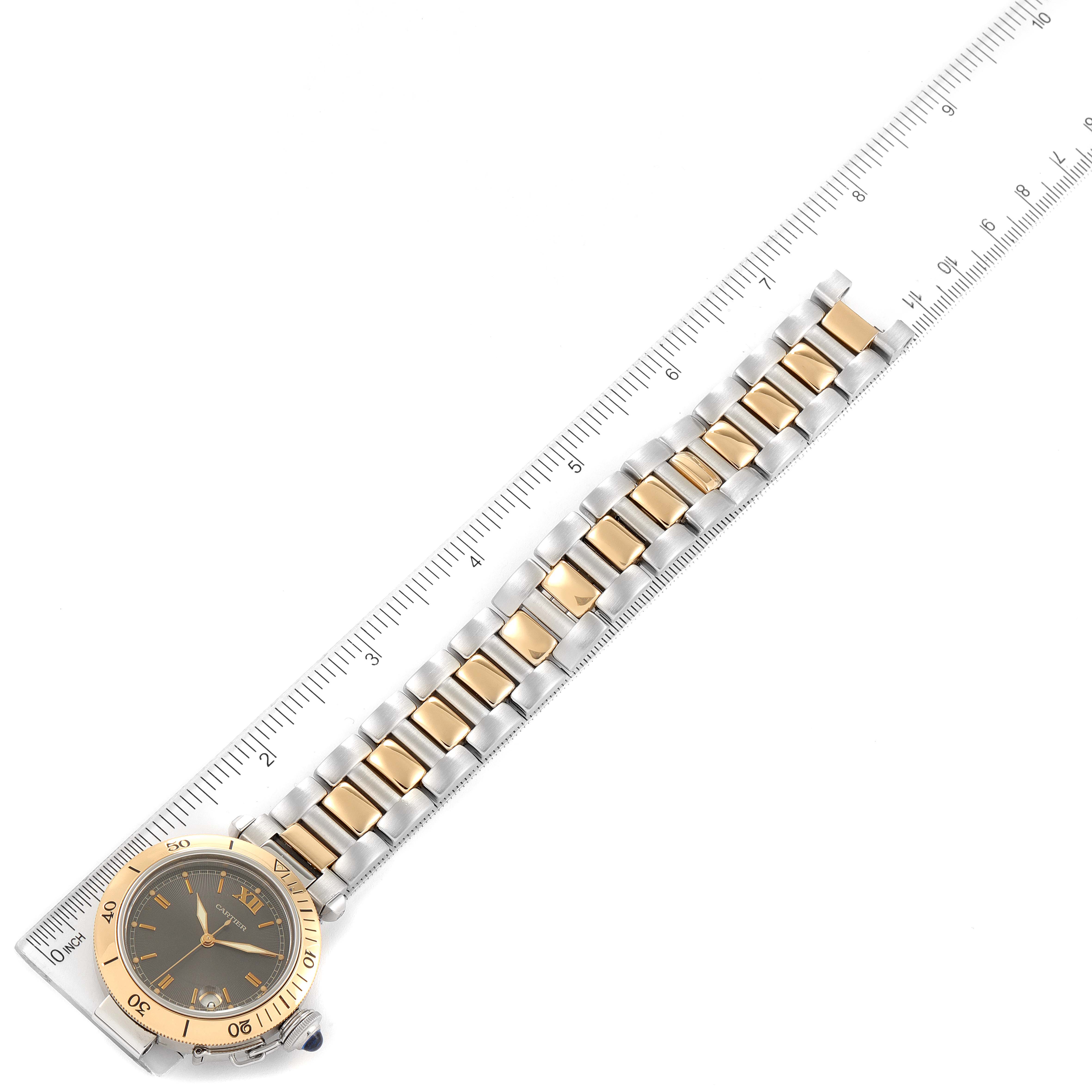 The Cartier Pasha W31016N1 Men
s Steel and Gold (two tone) Grey Dial W31016N1 Men
s Steel and Gold (two tone) Grey Dial watch is shown from a top view, highlighting the watch face and gold-and-silver bracelet against a measuring ruler.