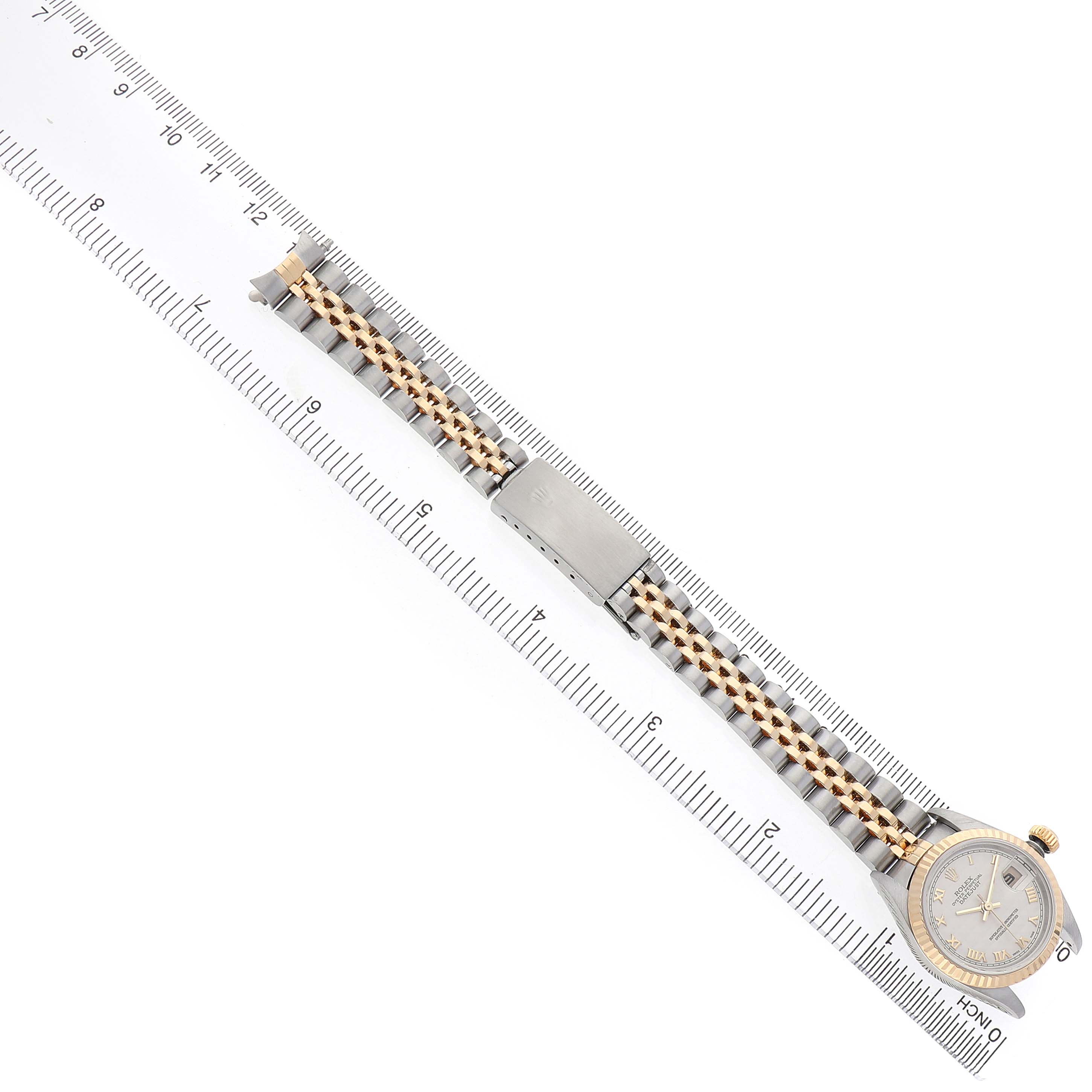 The Rolex Datejust 79173 Women's Steel and Gold (two tone) White Dial watch is shown from above, with its two-tone bracelet fully extended alongside a ruler.