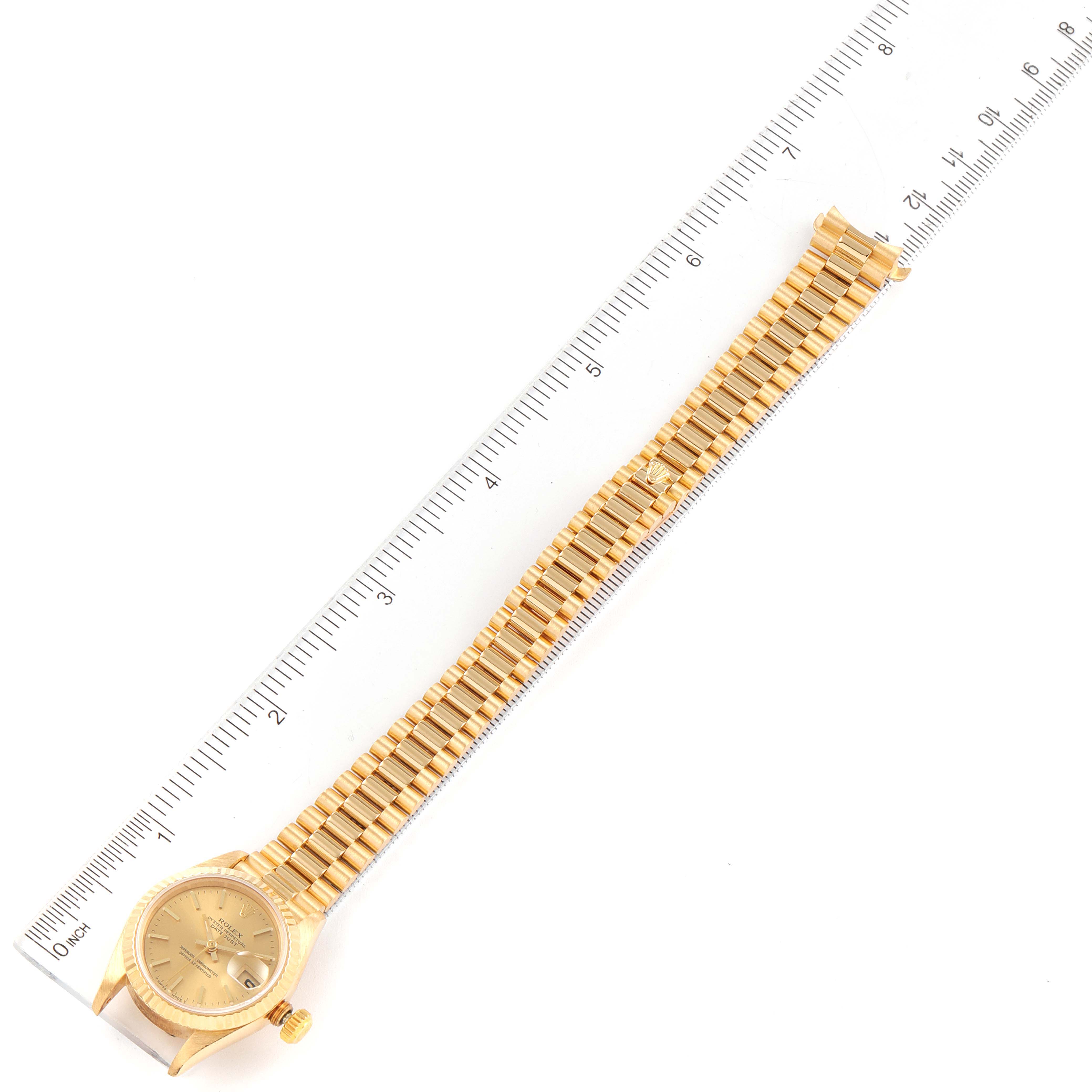 The Rolex President 69178 Women
s Yellow Gold Champagne Dial 69178 Women
s Yellow Gold Champagne Dial watch is shown from a top-down angle, displaying its gold case, dial, and full bracelet alongside a ruler for scale.
