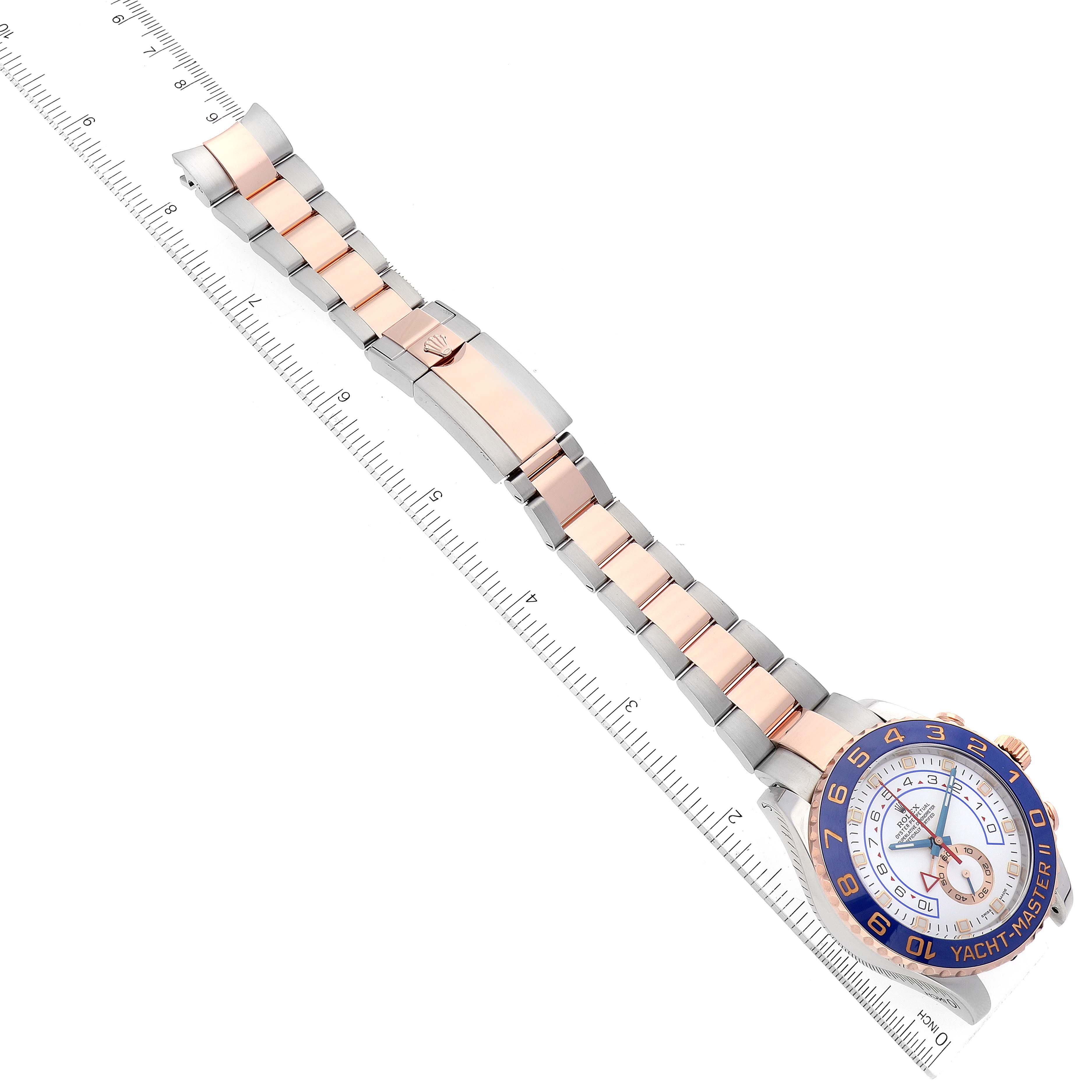 This image shows a Rolex Yacht-Master 116681 Men
s Steel and Gold (two tone) White Dial 116681 Men
s Steel and Gold (two tone) White Dial watch laid flat with a focus on its bracelet and face, alongside a ruler for measurement.