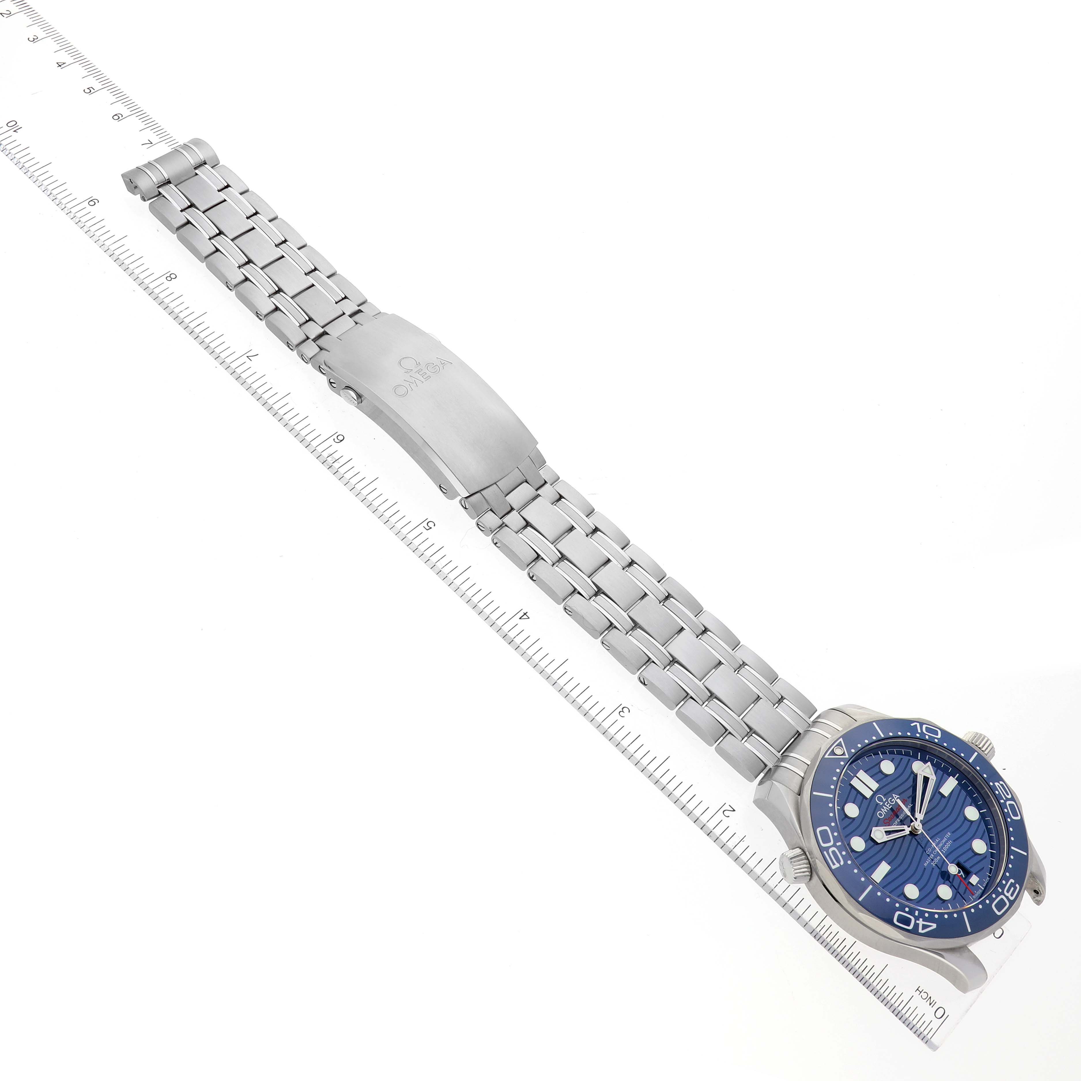 The Omega Seamaster 210.30.42.20.03.001 Men's Stainless Steel Blue Dial 210.30.42.20.03.001 Men's Stainless Steel Blue Dial watch is shown from an angled top view, displaying the face, bezel, bracelet, clasp, and aligned with a ruler for scale.