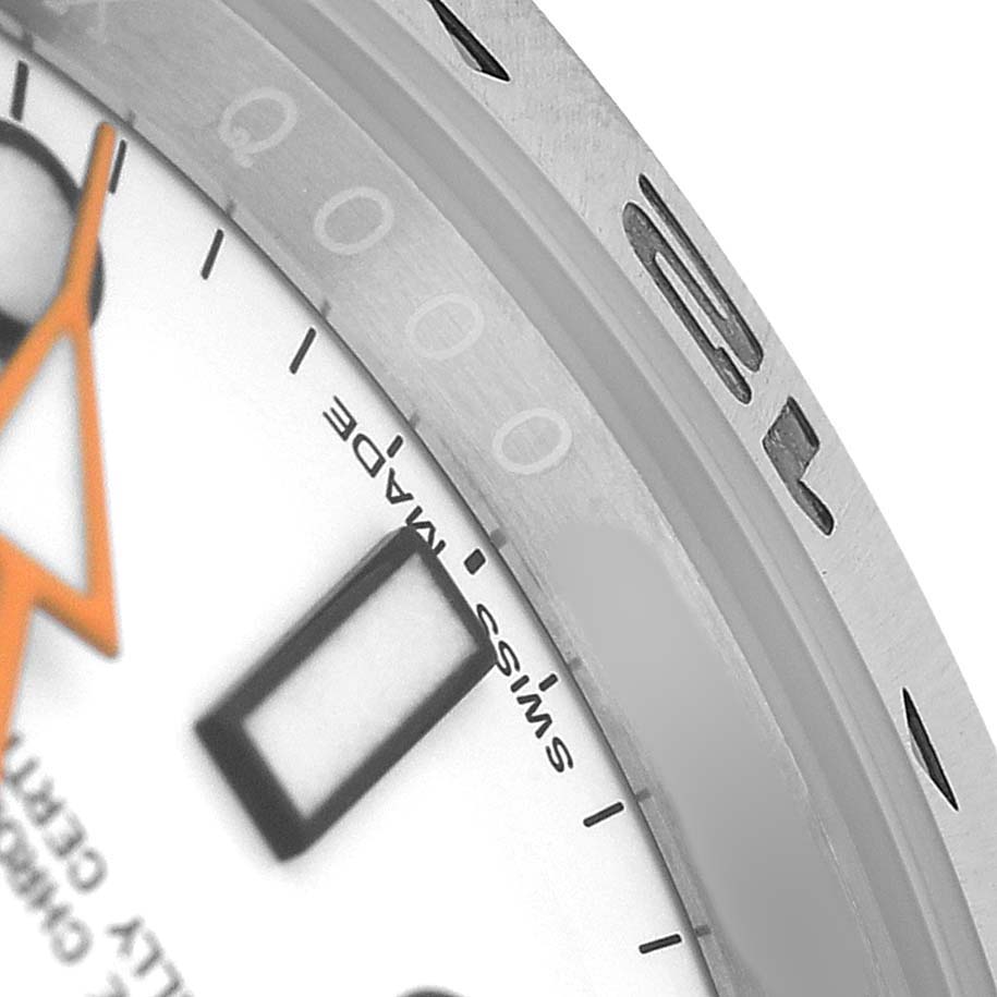 The image shows a close-up of the bezel and dial of a Rolex Explorer 216570 Men's Stainless Steel White Dial watch, highlighting the "Swiss Made" marking and part of the orange hand.