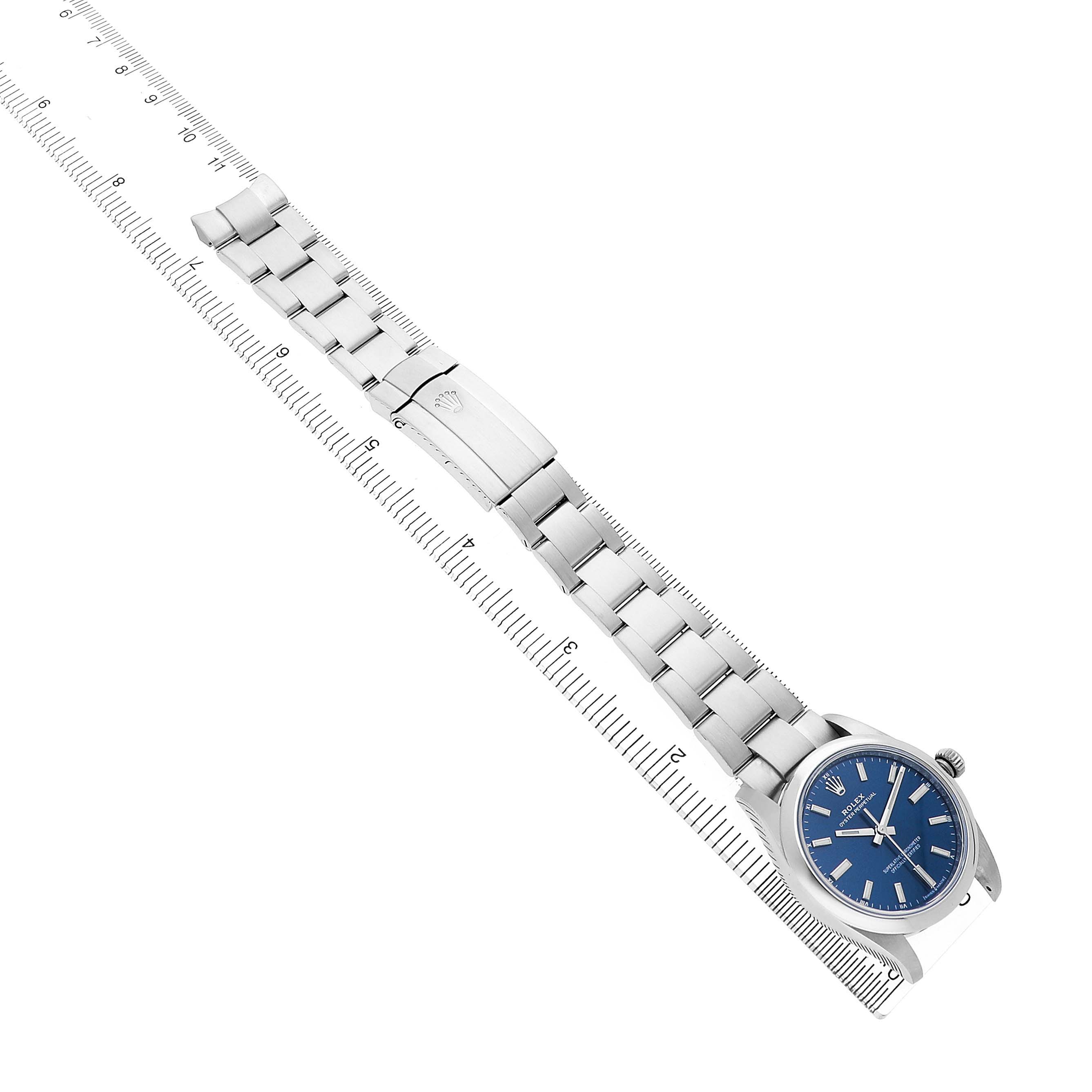 The Rolex Oyster Perpetual 124200 Men's Stainless Steel Blue Dial watch is shown from a top view, highlighting the silver bracelet, clasp, and blue watch face alongside a ruler.