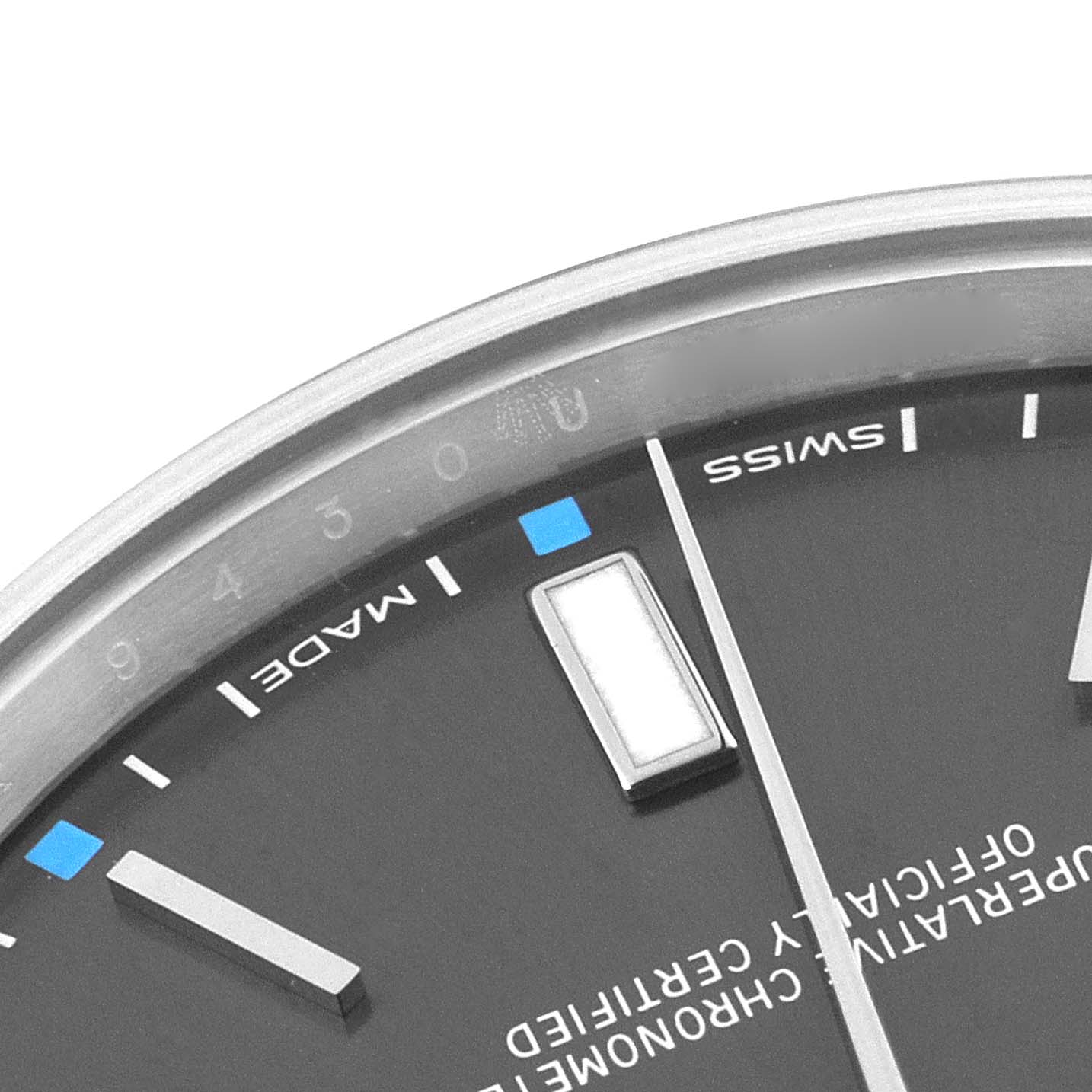 The image shows a close-up angle of the Rolex Oyster Perpetual 114300 Men's Stainless Steel Grey Dial 114300 Men's Stainless Steel Grey Dial watch face, highlighting its indices and part of the dial text.