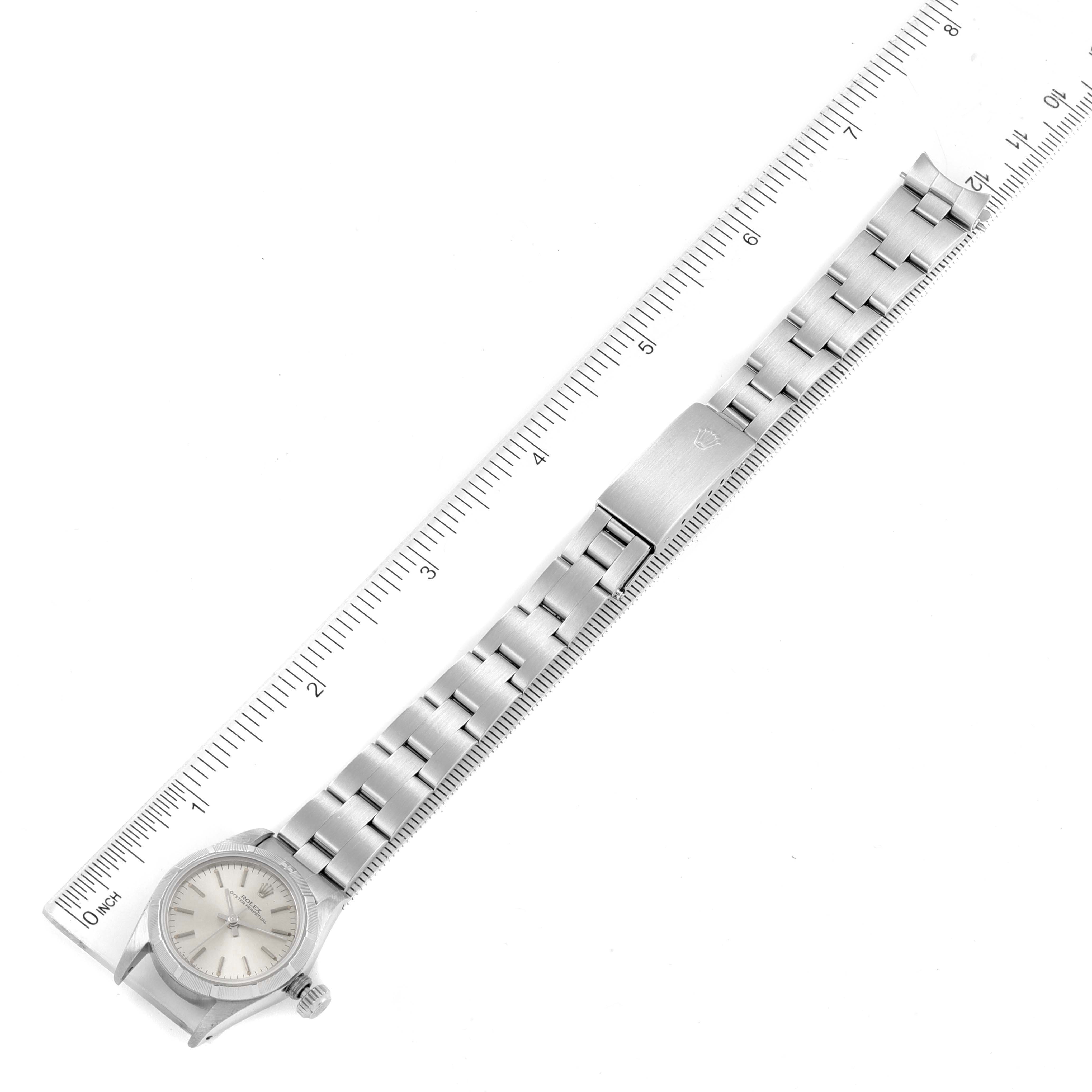 The image shows a top-down view of a Rolex Oyster Perpetual 67230 Women
s Stainless Steel Silver Dial 67230 Women
s Stainless Steel Silver Dial watch with a metal bracelet and a ruler for scale.