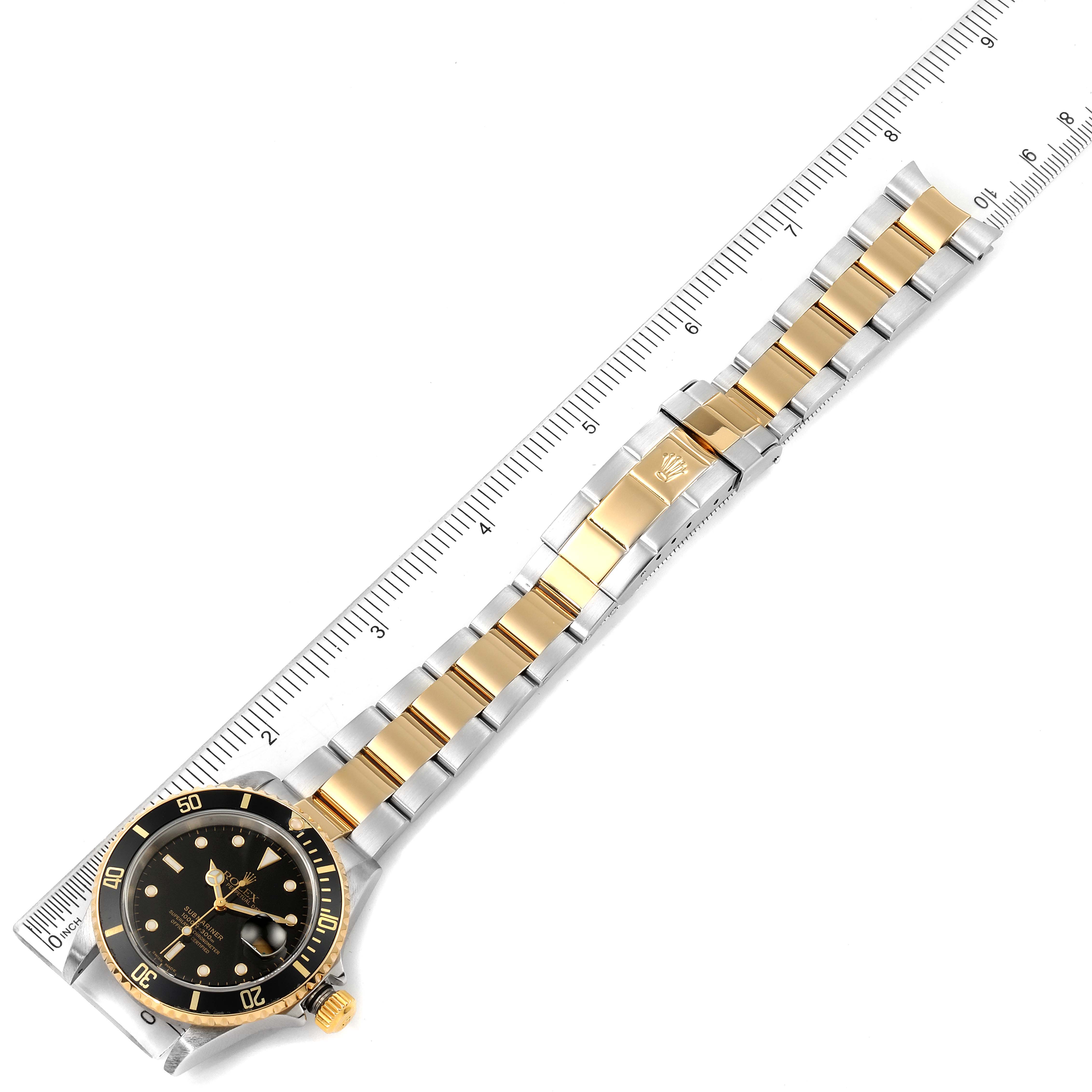 The image shows a top view of a Rolex Submariner 16613 Men's Steel and Gold (two tone) Black Dial 16613 Men's Steel and Gold (two tone) Black Dial watch, focusing on the face and gold and silver bracelet, displayed along a ruler.