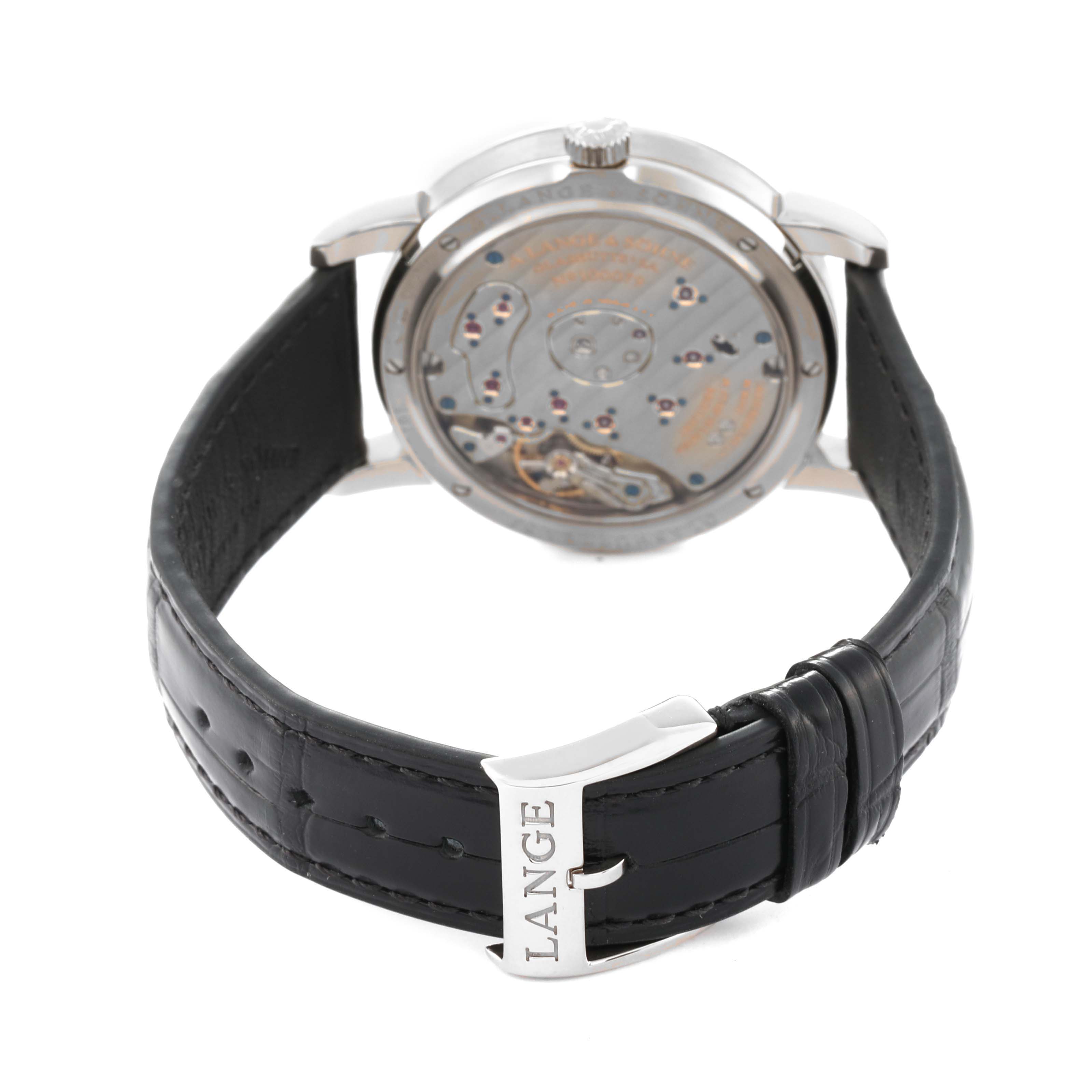 The image shows the back view of an A. Lange & Sohne Lange 1 101.039 Men's White Gold Silver Dial watch, displaying its movement, black leather strap, and buckle.
