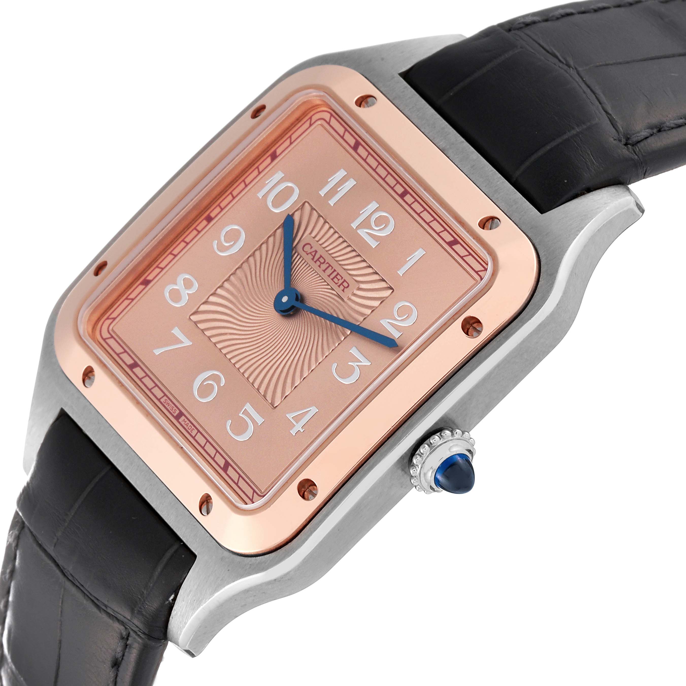 The image shows a Cartier Santos Dumont W2SA0025 Men
s Stainless Steel Pink Dial W2SA0025 Men
s Stainless Steel Pink Dial watch with a rose-gold square face and black leather strap from an angle displaying the dial and crown.