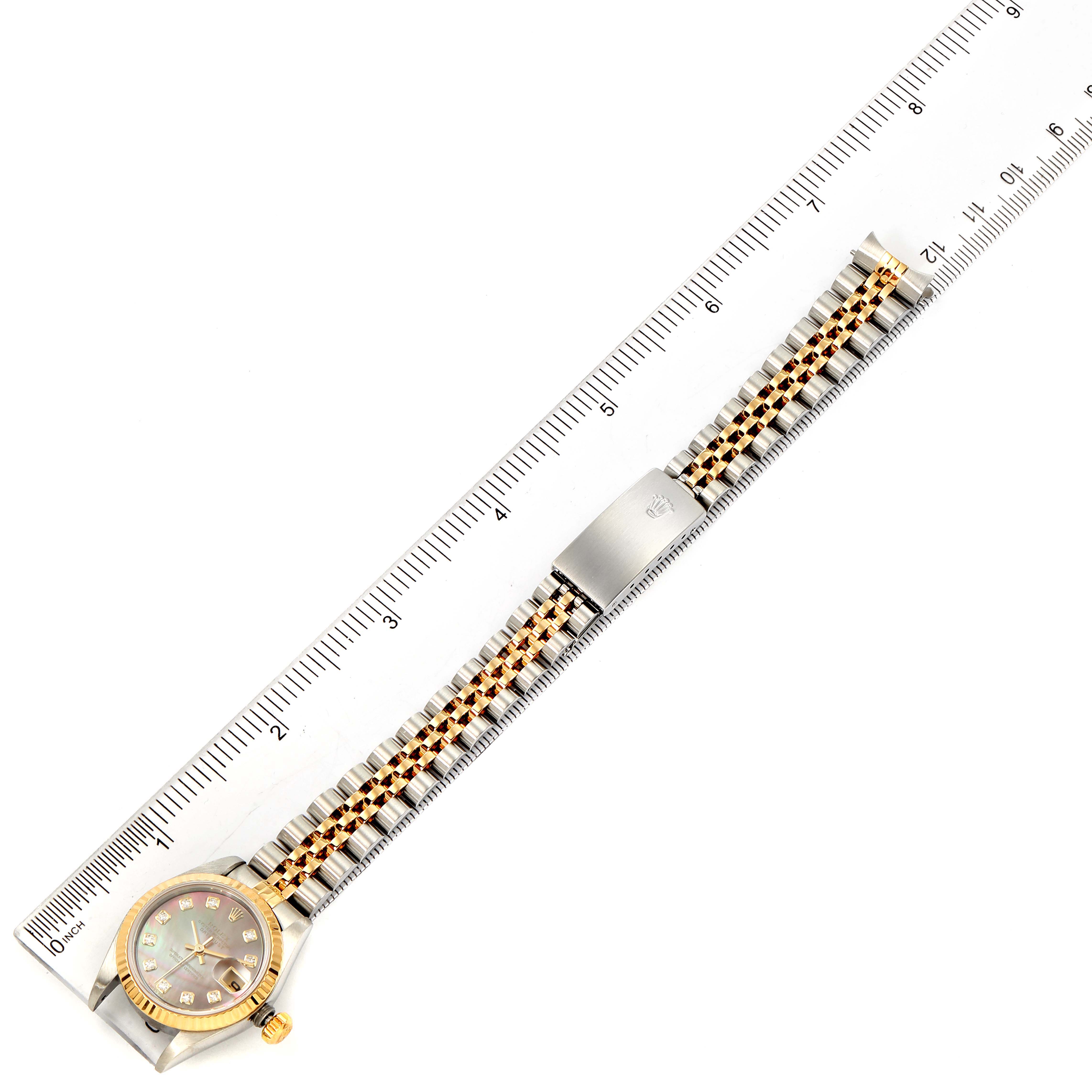 This image displays a Rolex Datejust 79173 Women's Steel and Gold (two tone) Mother of Pearl Dial 79173 Women's Steel and Gold (two tone) Mother of Pearl Dial watch laid flat next to a ruler, clearly showing the bracelet, clasp, and face.