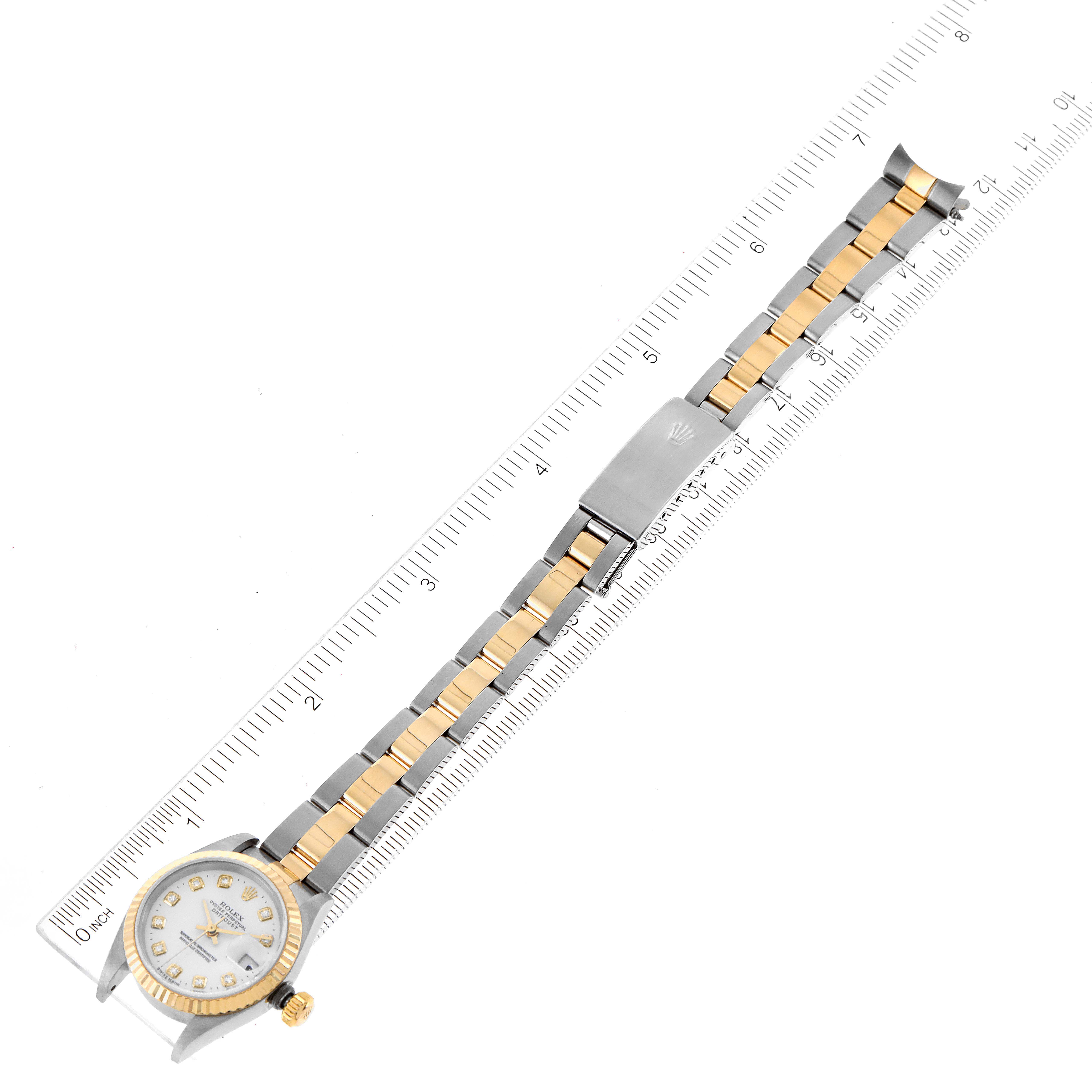 The image shows a Rolex Datejust 79173 Women
s Steel and Gold (two tone) White Dial 79173 Women
s Steel and Gold (two tone) White Dial watch placed on a ruler, displaying the face, bracelet, and clasp from a top-down angle.