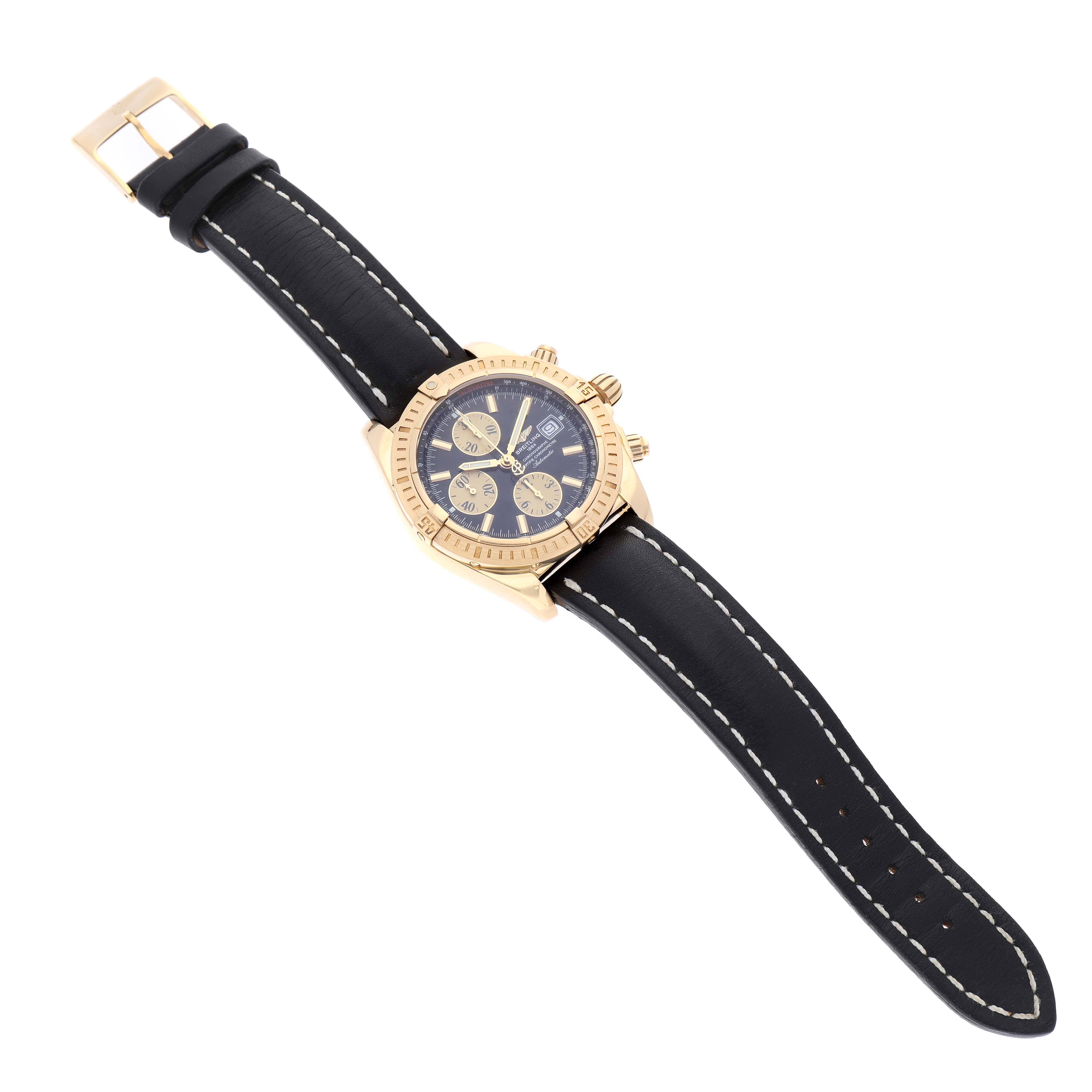 The Breitling Chronomat K13356 Men
s Yellow Gold Black Dial K13356 Men
s Yellow Gold Black Dial watch is shown at a slight angle, displaying its black strap, gold case, and dial with sub-dials.
