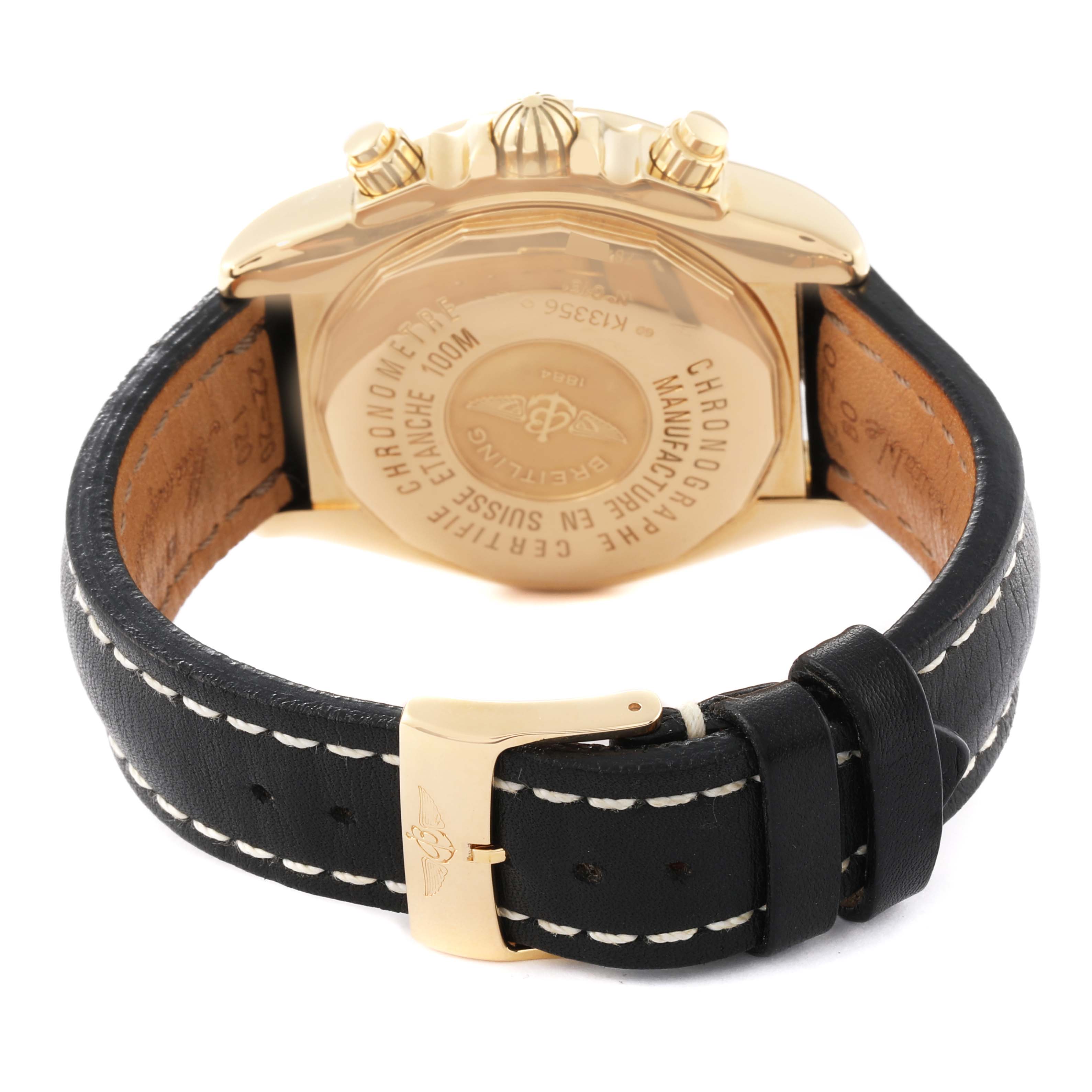 The image shows the back of a Breitling Chronomat K13356 Men
s Yellow Gold Black Dial K13356 Men
s Yellow Gold Black Dial watch, focusing on the case back, crown, pushers, and black leather strap with stitching.