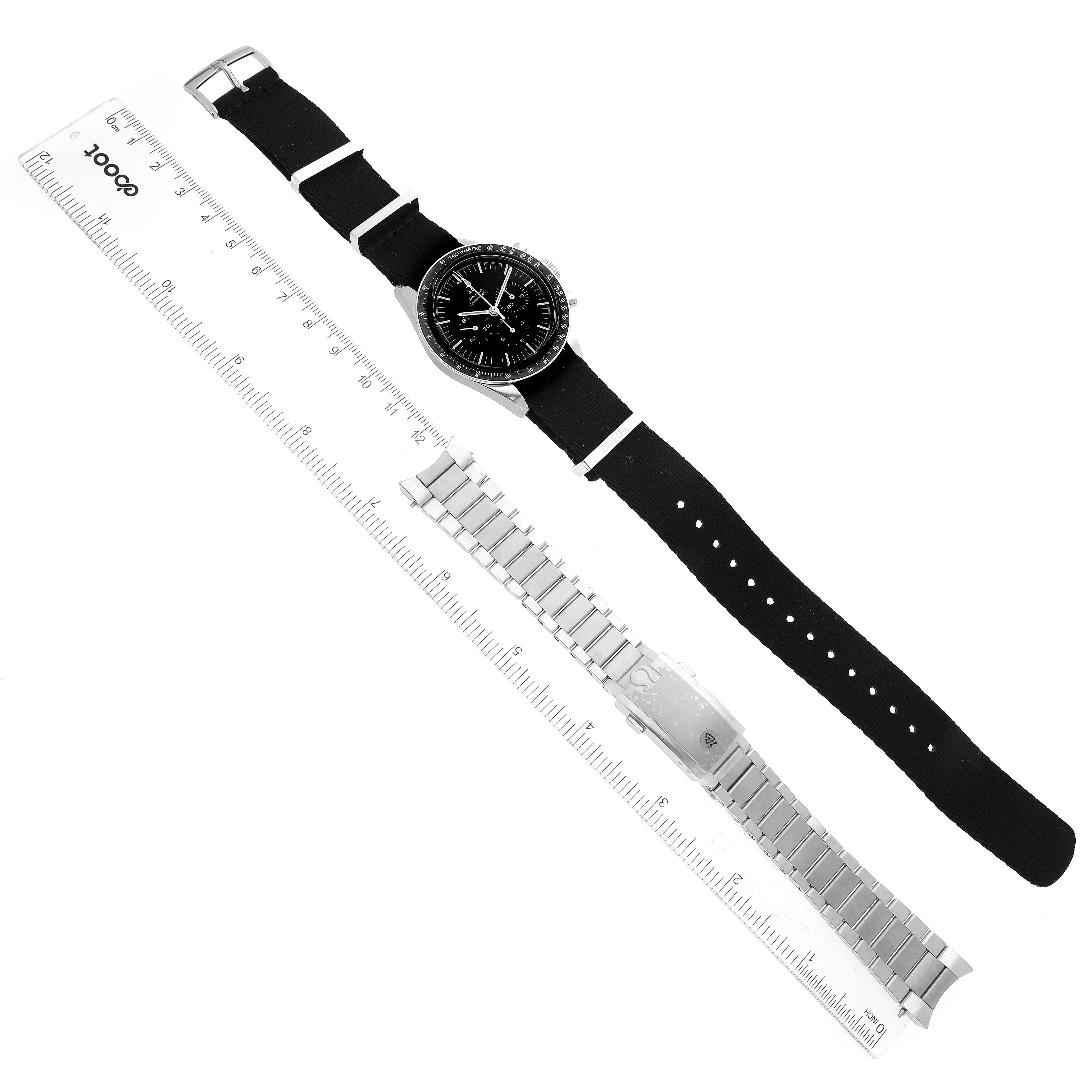 The image shows an Omega Speedmaster 311.30.40.30.01.001 Men
s Stainless Steel Black Dial 311.30.40.30.01.001 Men
s Stainless Steel Black Dial watch with a fabric strap, a metal bracelet, and rulers, viewed from above.