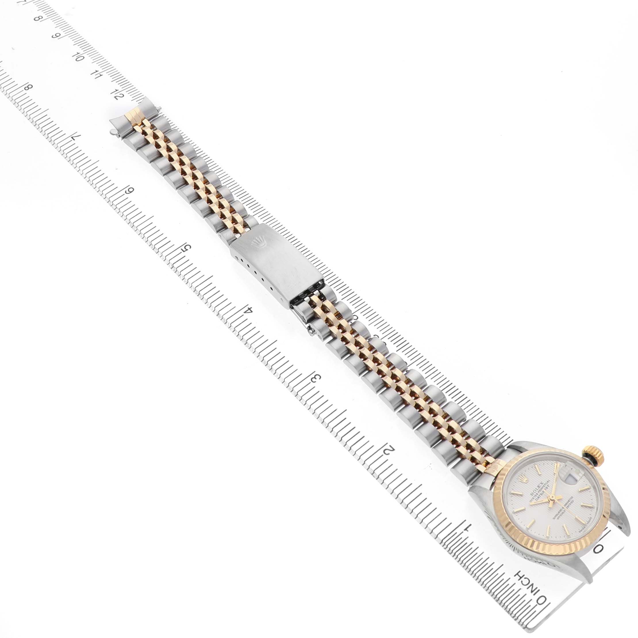 The Rolex Datejust 79173 Women's Steel and Gold (two tone) Silver Dial watch is shown from a top view, displaying the dial, bracelet, and clasp aligned with a ruler for scale.