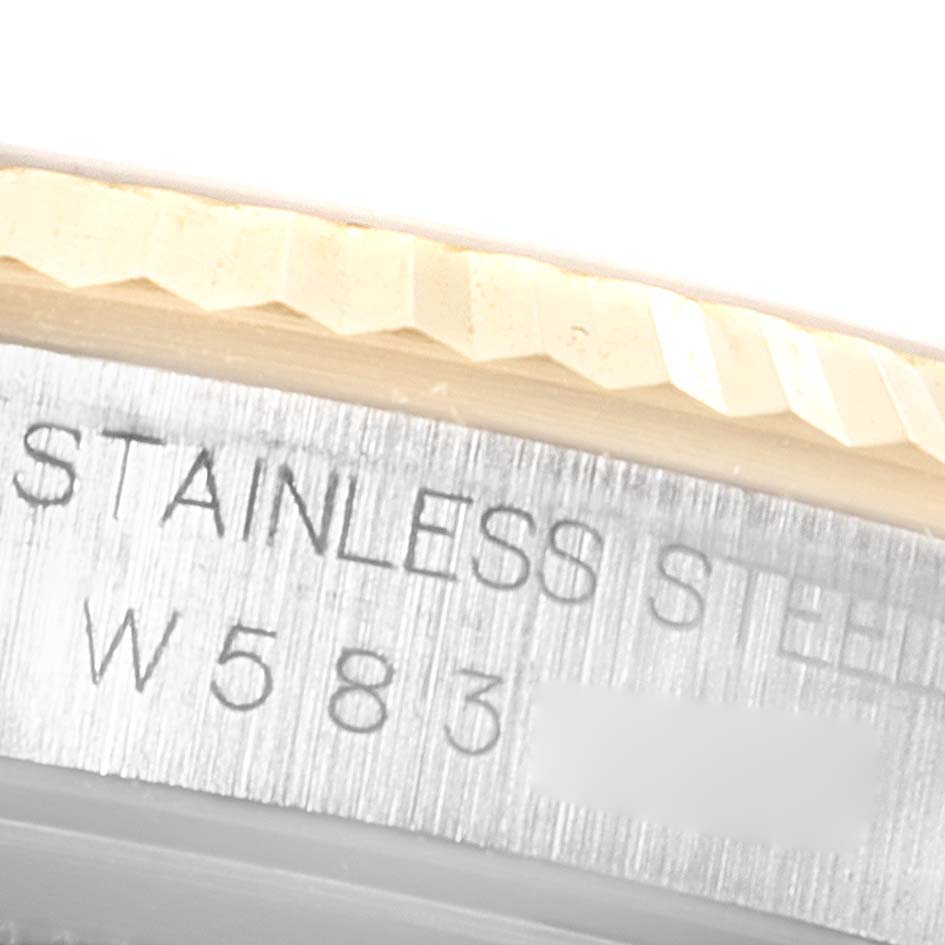 The image shows a close-up of the Rolex Datejust 16233 Men's Steel and Gold (two tone) Champagne Dial 16233 Men's Steel and Gold (two tone) Champagne Dial model's fluted bezel and a part of the stainless steel case with an engraved serial number.