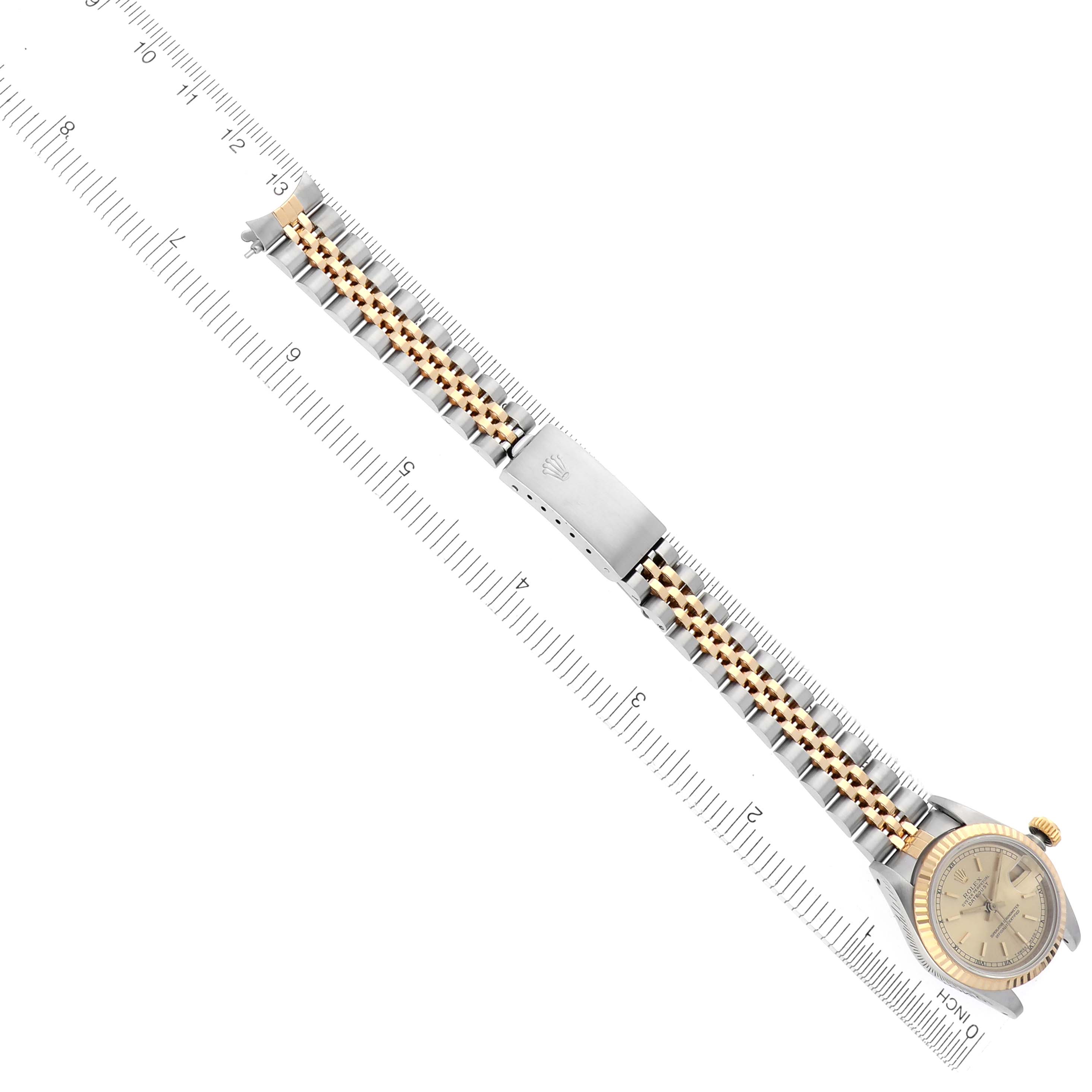 The Rolex Datejust 69173 Women's Steel and Gold (two tone) Champagne Dial 69173 Women's Steel and Gold (two tone) Champagne Dial watch is shown from a top view, highlighting the dial, bracelet, and clasp against a ruler backdrop.