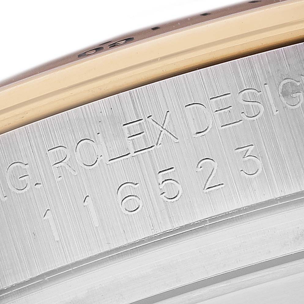 The image shows a close-up of the engraved serial number and "Rolex Design" text on the side of a Rolex Daytona 116523 Men's Steel and Gold (two tone) Mother of Pearl Dial 116523 Men's Steel and Gold (two tone) Mother of Pearl Dial watch case.