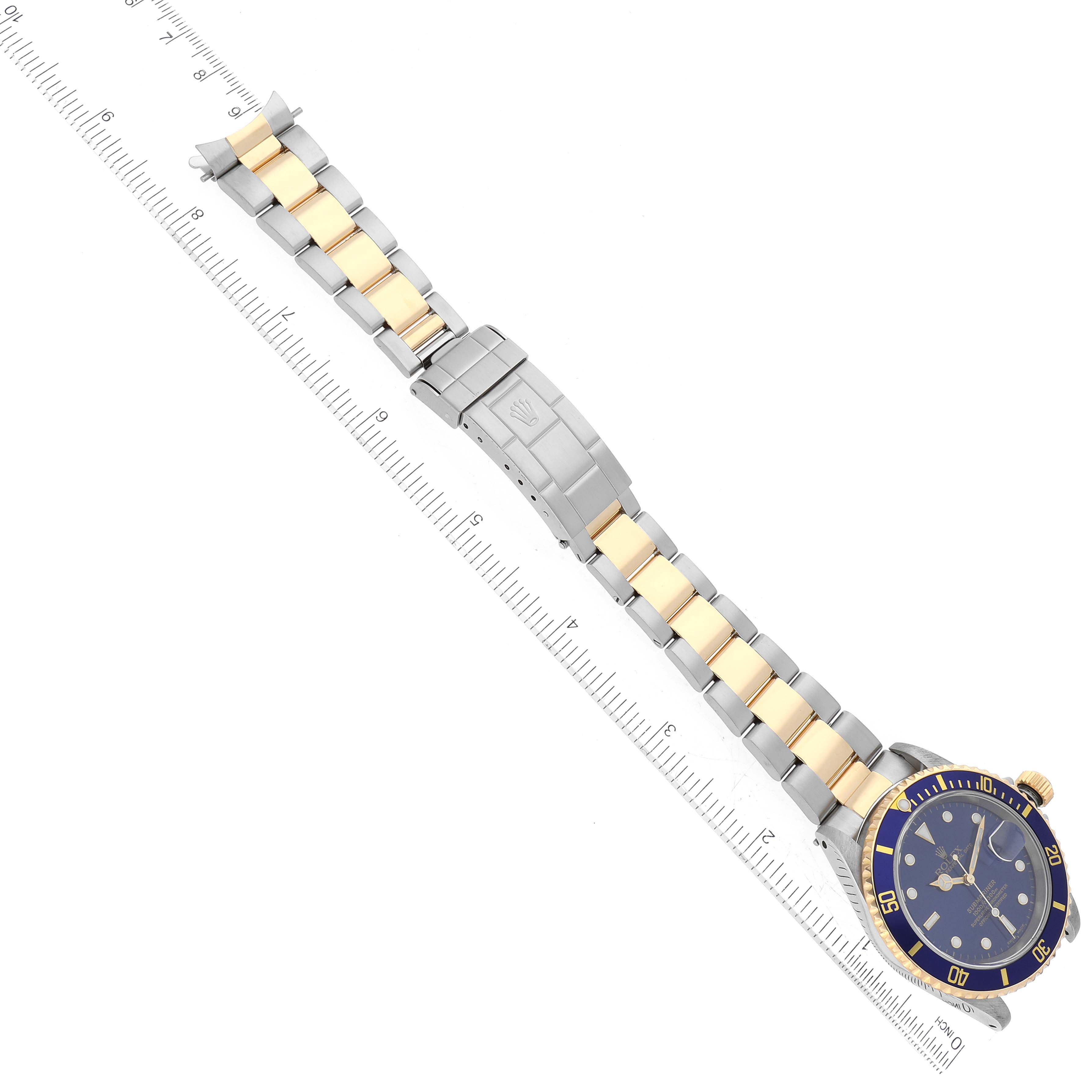 The image shows the full length of a Rolex Submariner 16613 Men's Steel and Gold (two tone) Blue Dial 16613 Men's Steel and Gold (two tone) Blue Dial watch, from an angled top view, including its blue and gold dial, bezel, and two-tone bracelet.