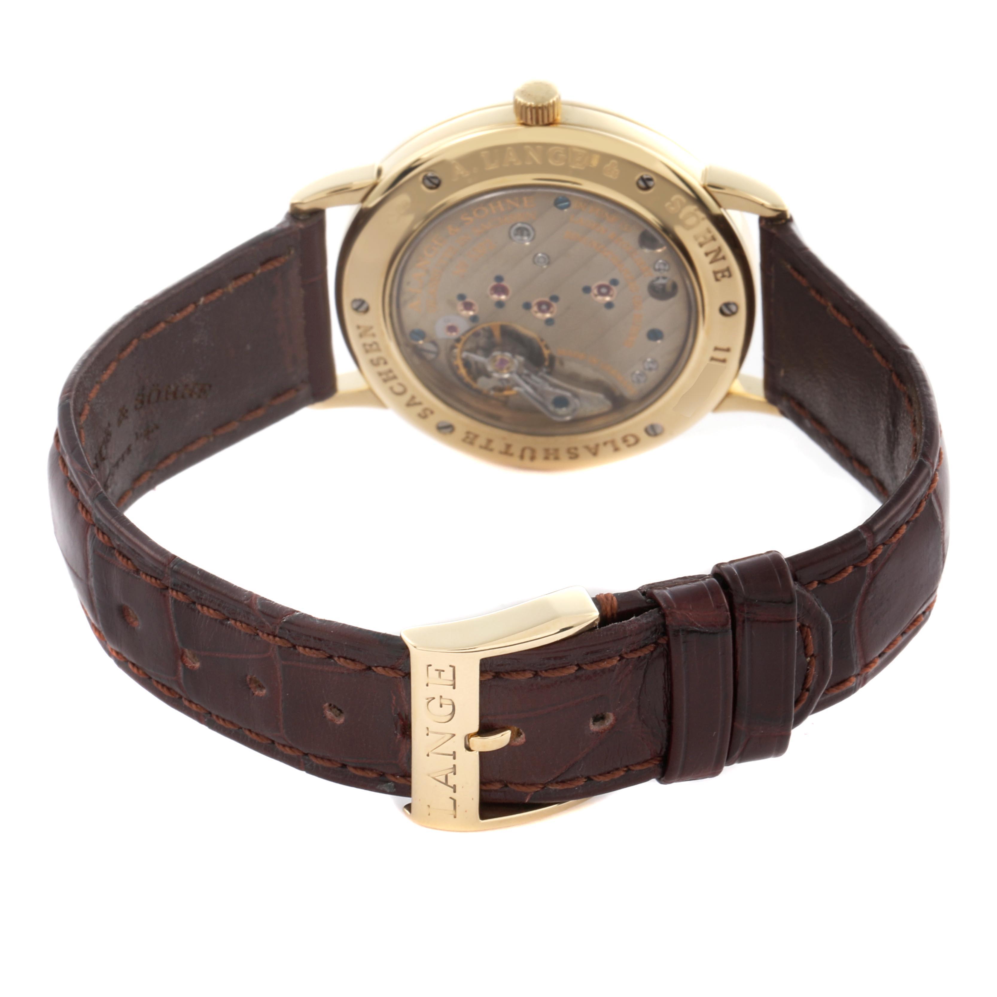 The image shows the back of the A. Lange & Sohne 1815 206.021 Men's Yellow Gold Silver Dial watch, highlighting its movement and brown leather strap.