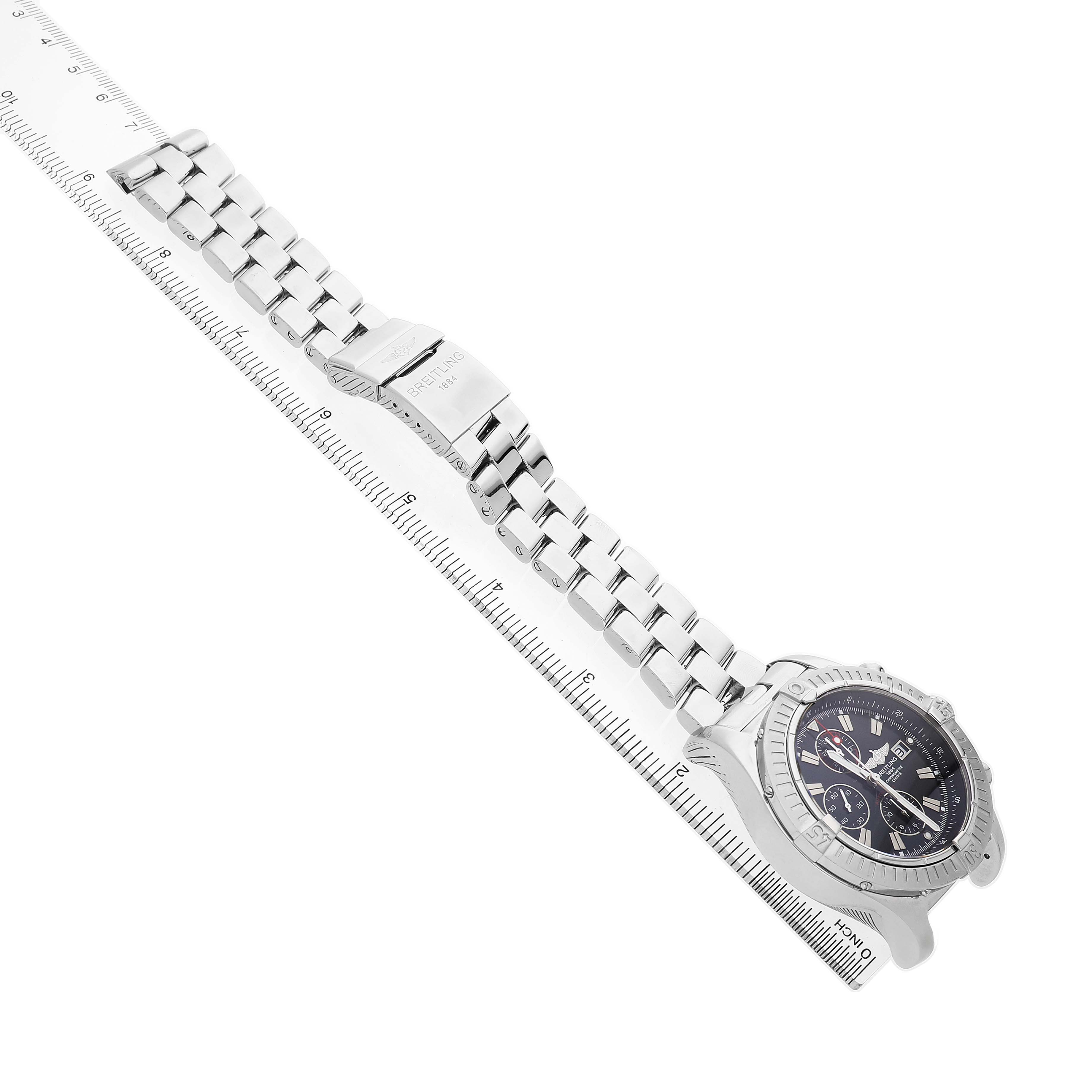 The Breitling Avenger A1337011 / B907 Men's Stainless Steel Black Dial watch is shown from an overhead angle, highlighting the dial, bezel, and metal bracelet on a measuring scale.