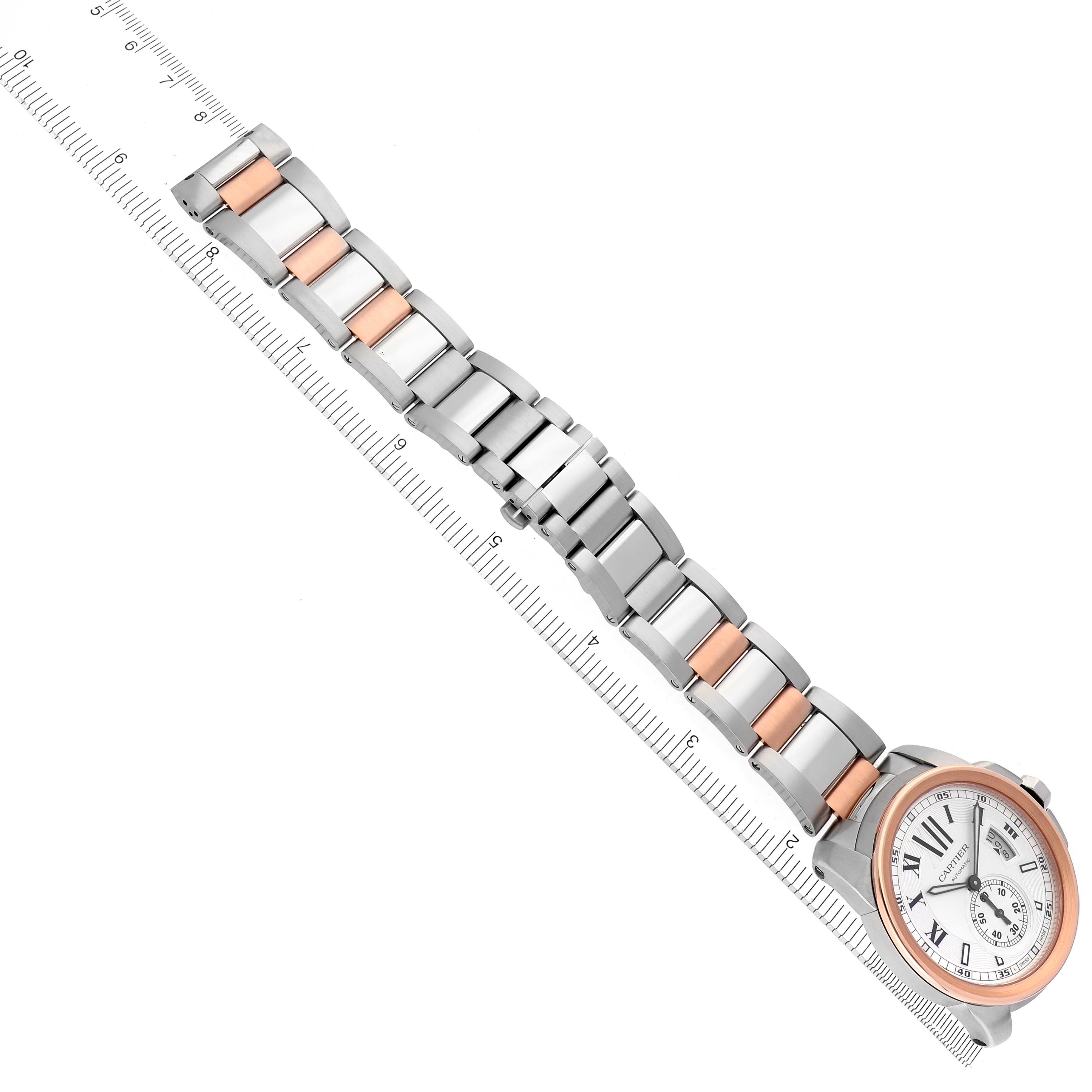 The image shows a top view of the full length of a Calibre de Cartier watch by Cartier, including the face and two-tone metal bracelet next to a ruler.
