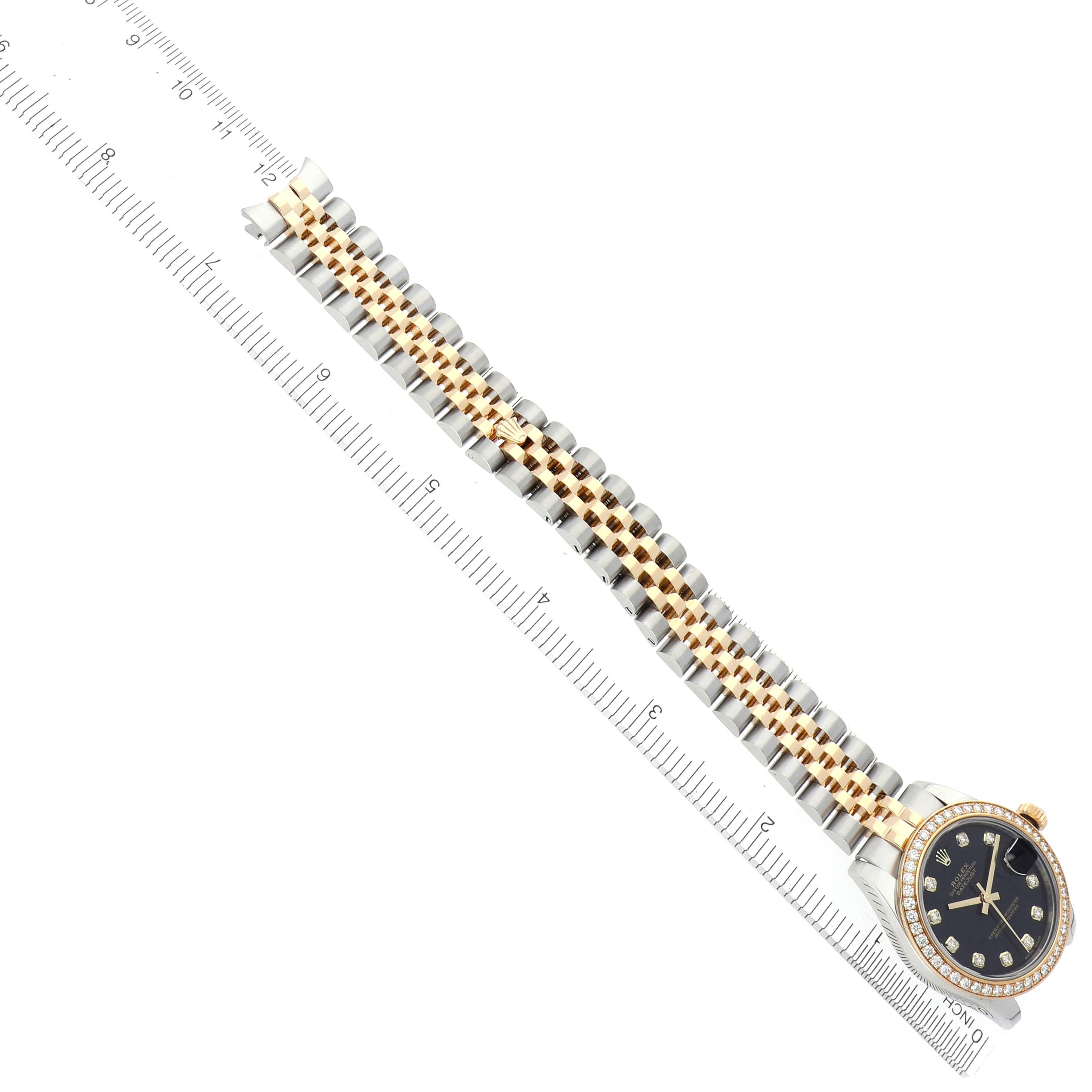The Rolex Mid-Size 178383 Women's Steel and Gold (two tone) Black Dial 178383 Women's Steel and Gold (two tone) Black Dial watch is displayed diagonally showing the dial, bezel, and full two-tone bracelet beside a ruler.