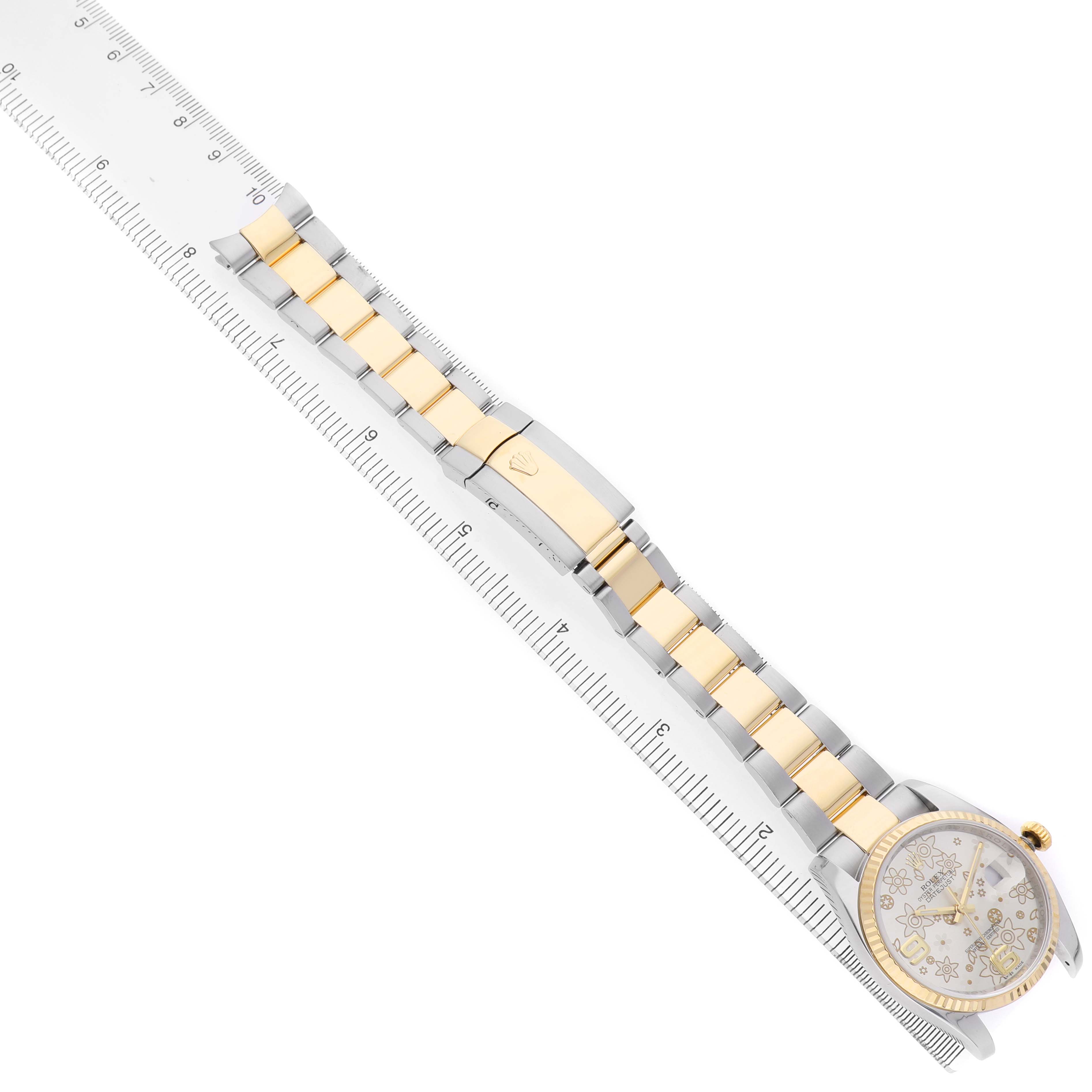 The Rolex Datejust 116233 Men's Steel and Gold (two tone) Silver Dial watch is shown from an overhead angle, displaying the face, bracelet, and clasp alongside a ruler for scale.